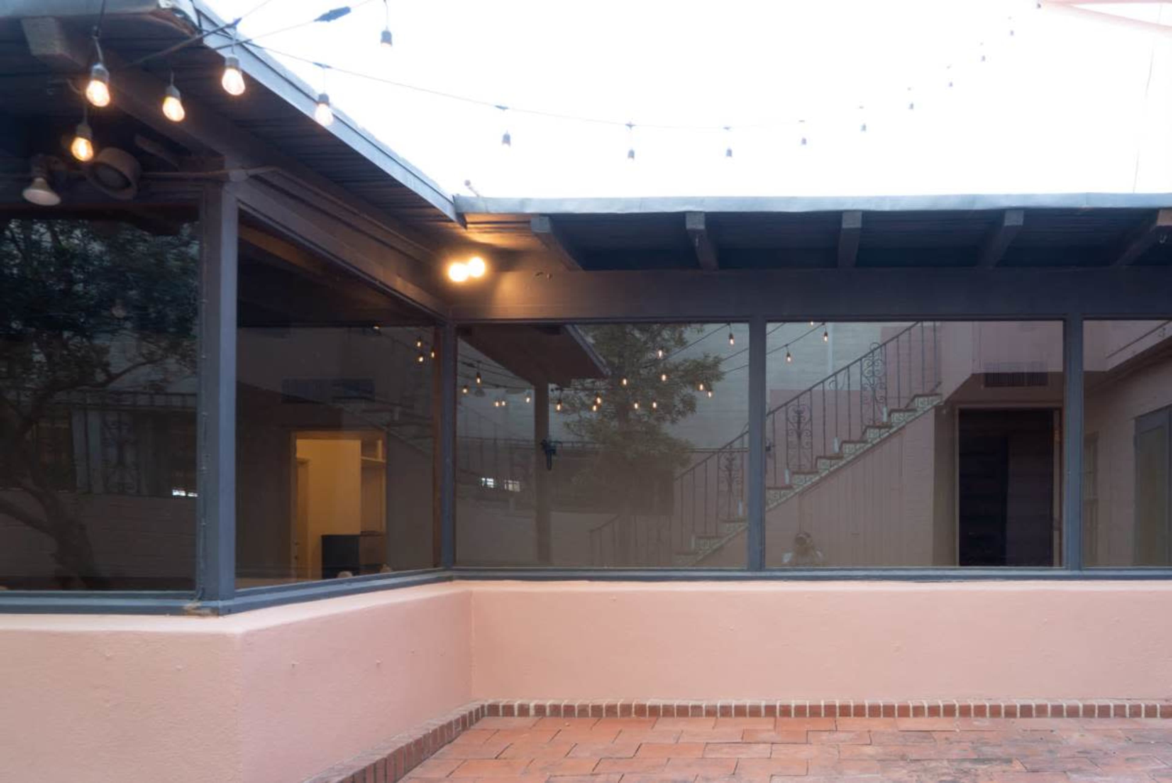 The image shows a patio area with a view of a glass wall reflecting string lights above and a staircase in the background.