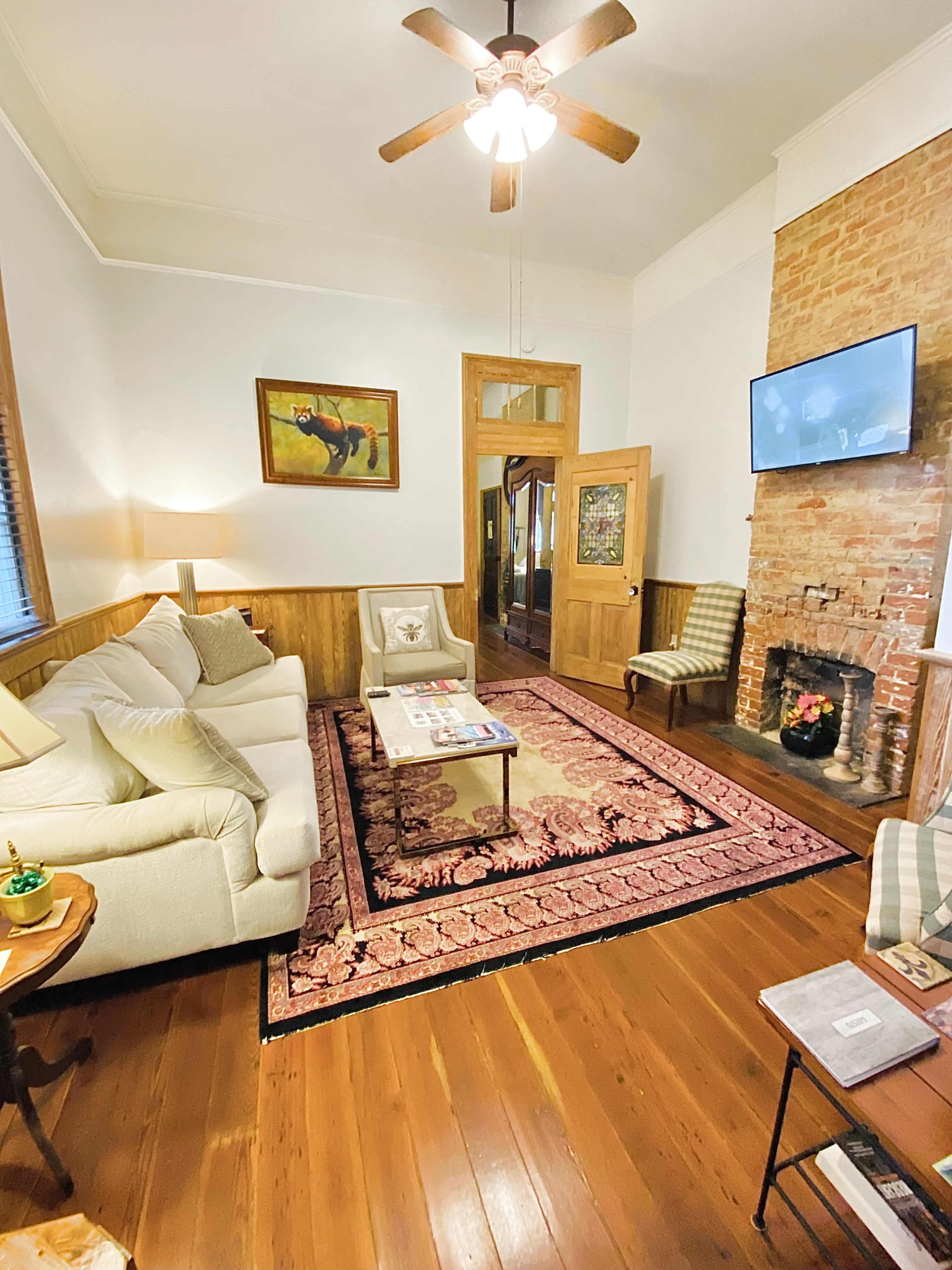 The cozy living room features a white sofa, a coffee table, a decorative rug, and a brick fireplace with a TV mounted above it.