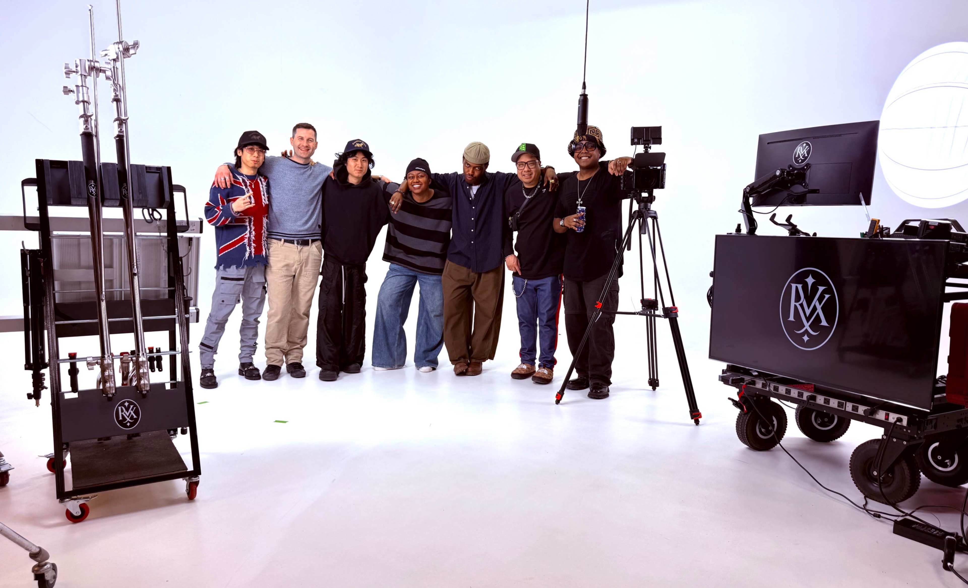 A group of seven individuals poses together in a studio setting, surrounded by filming equipment.
