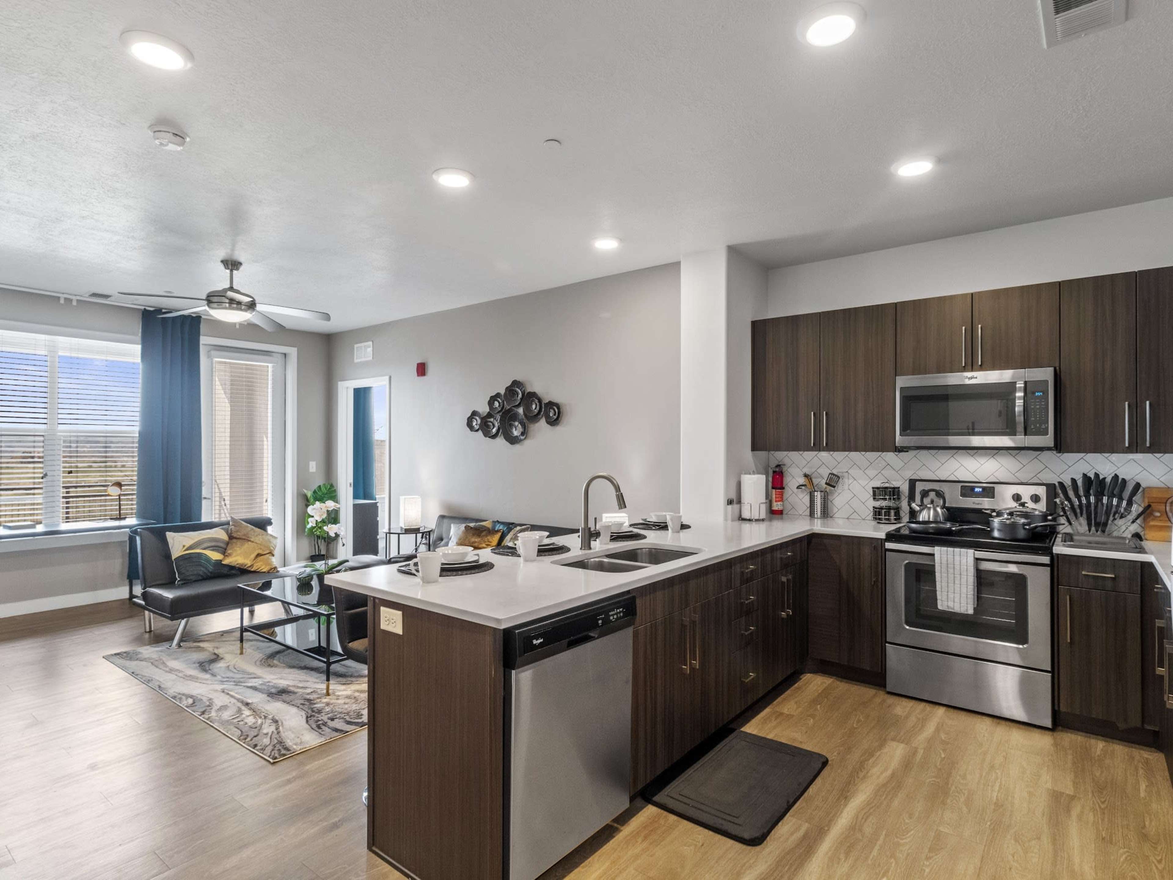 A modern kitchen area with dark wood cabinets, stainless steel appliances, and an adjacent living space featuring a couch and coffee table.