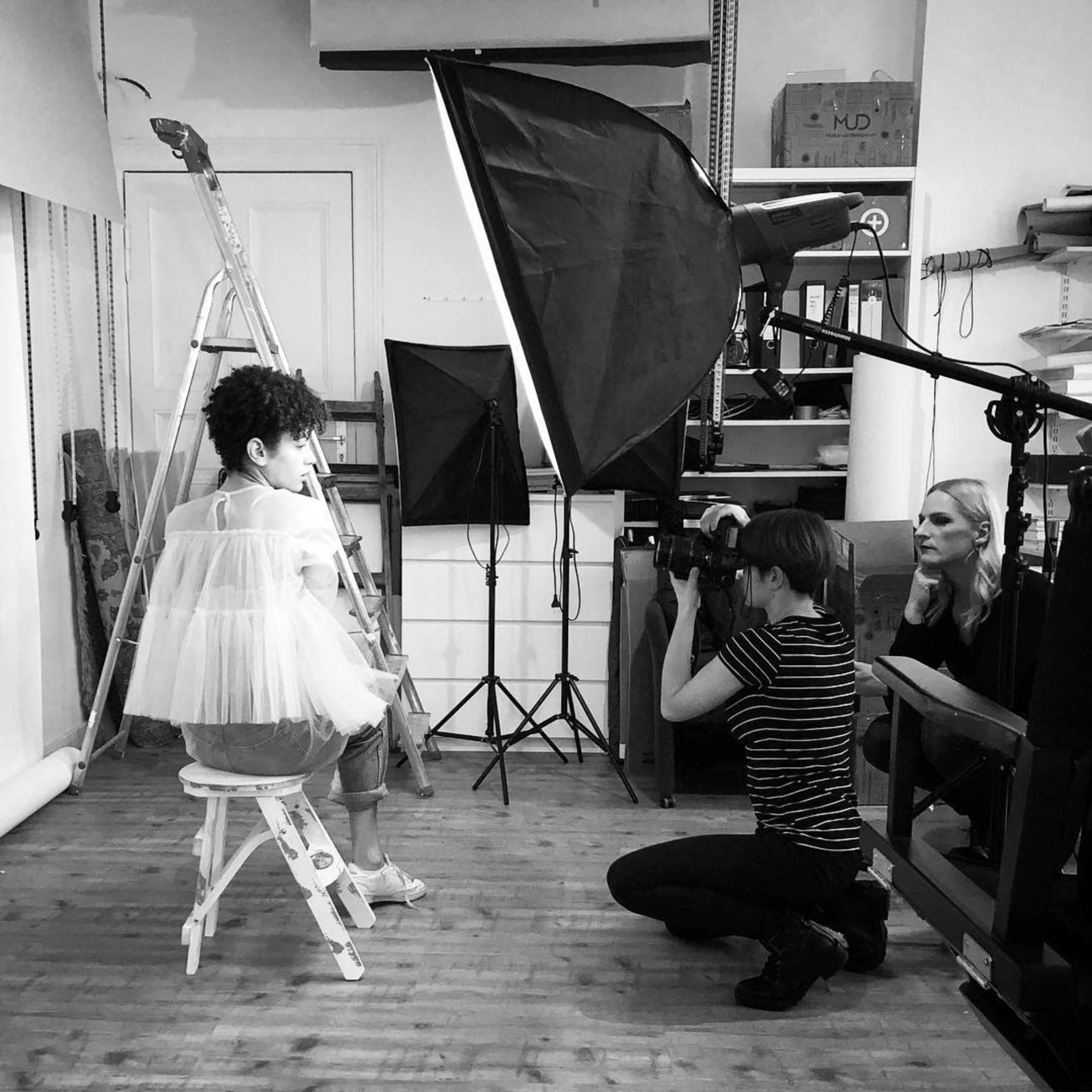 A photographer captures an image of a model posing on a stool in a well-lit studio.