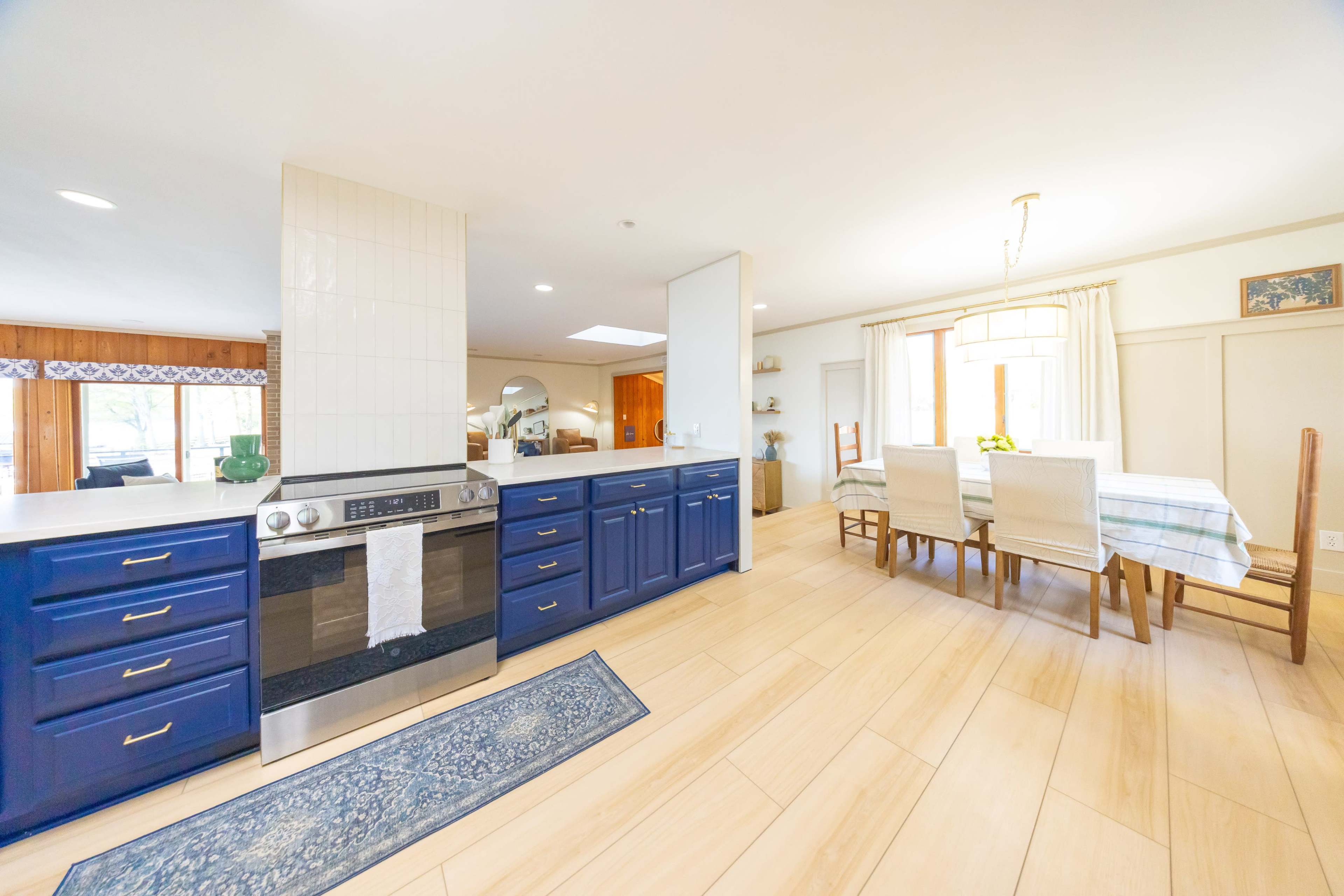 The image shows a spacious kitchen with blue cabinetry, an oven, and a dining area with a table and chairs in the adjacent room.