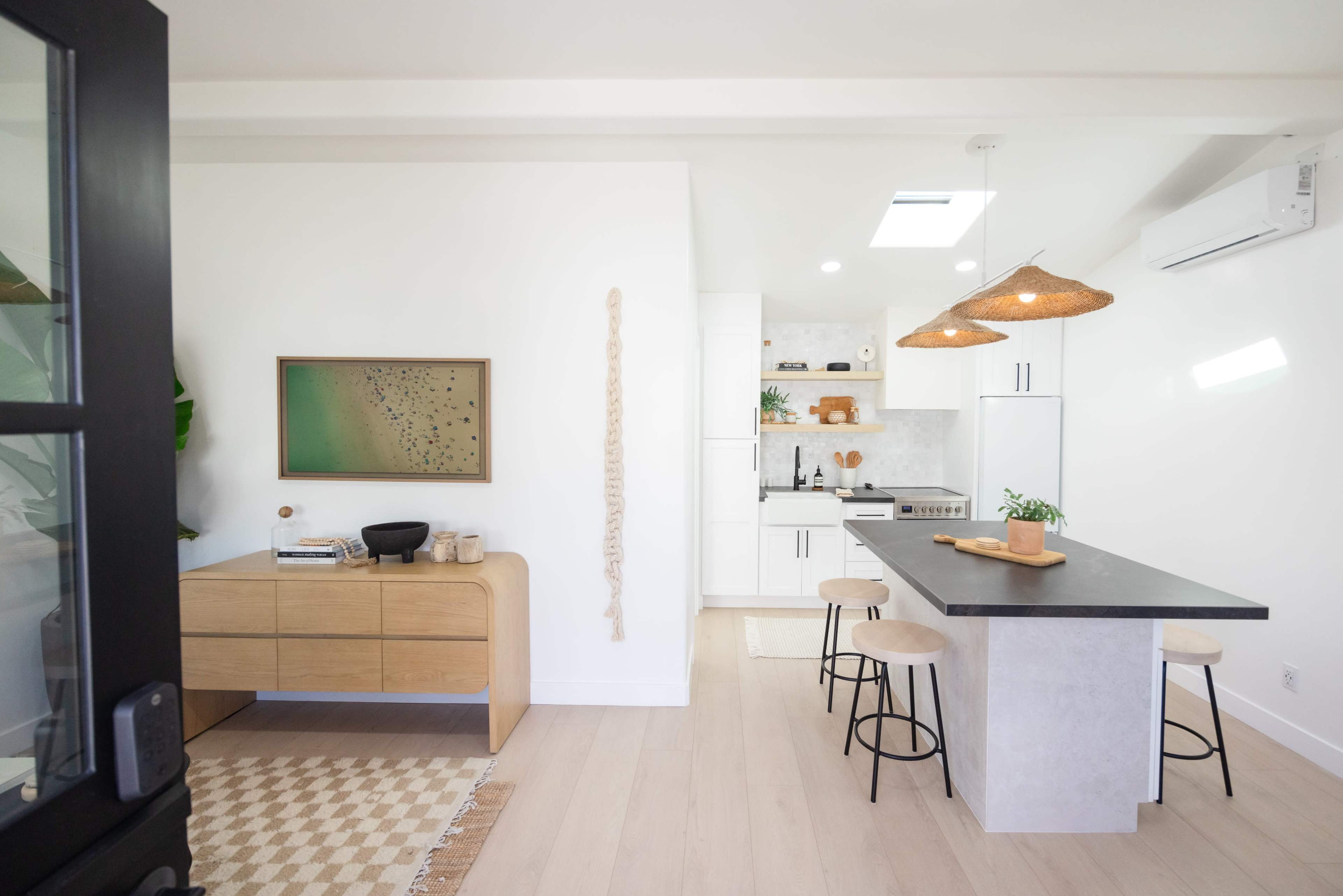 A modern kitchen and living area feature light wood furnishings, a black countertop island, and natural decor elements.