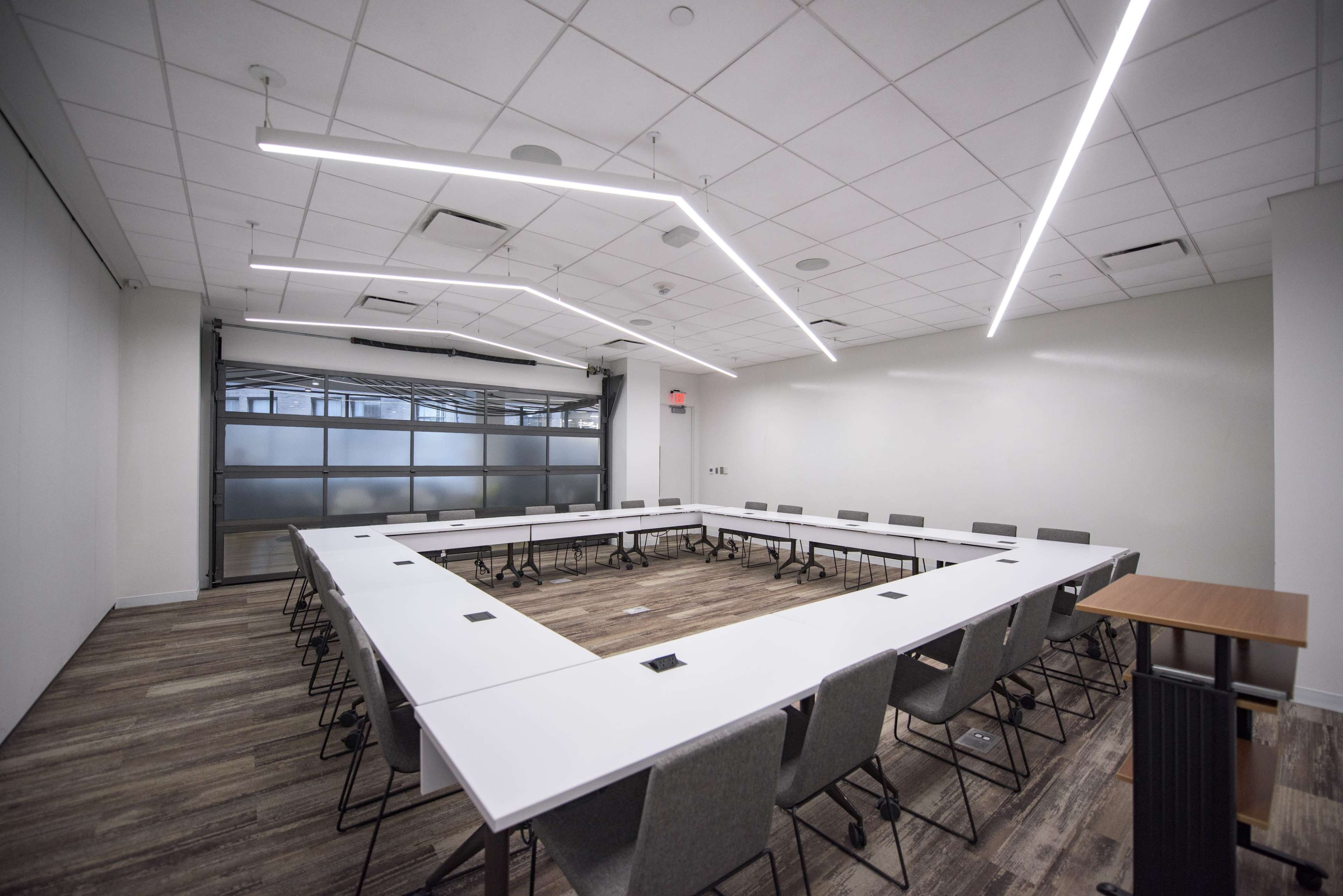 A modern conference room with a large rectangular table surrounded by chairs, and bright overhead lighting.