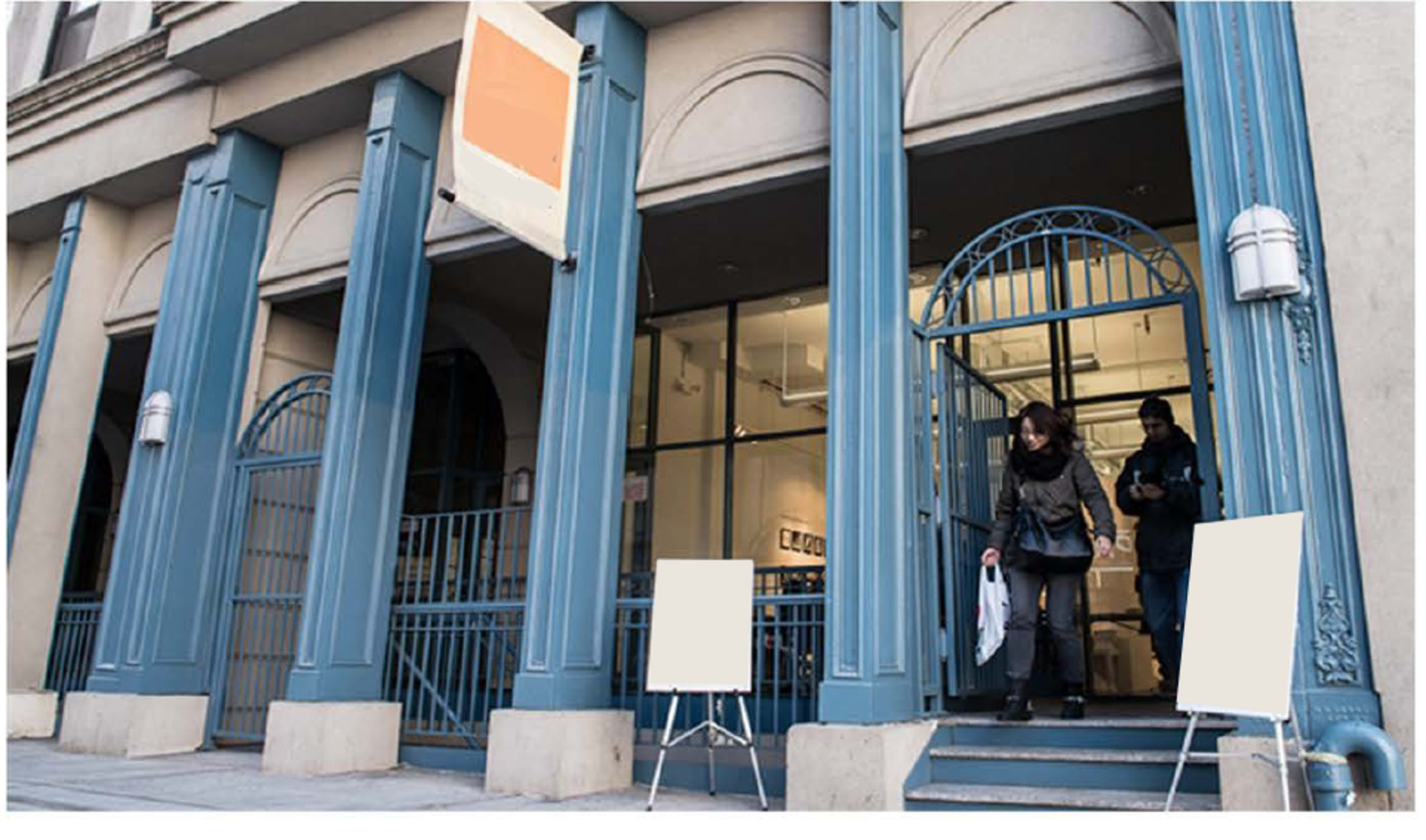 Two people exit a building with blue architectural features and blank signs outside.