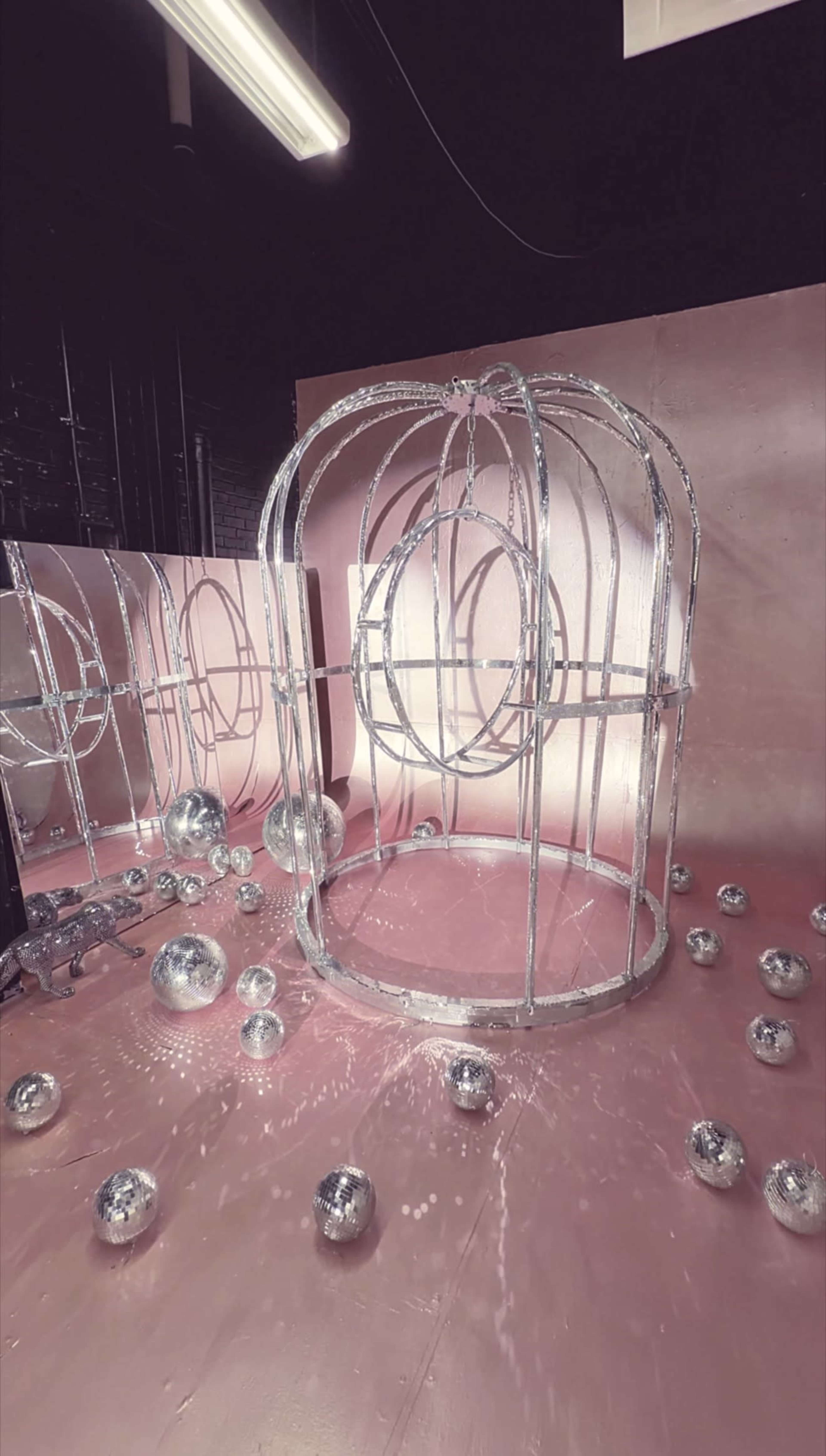 The scene features a metallic cage structure surrounded by scattered reflective spheres on a pink floor.