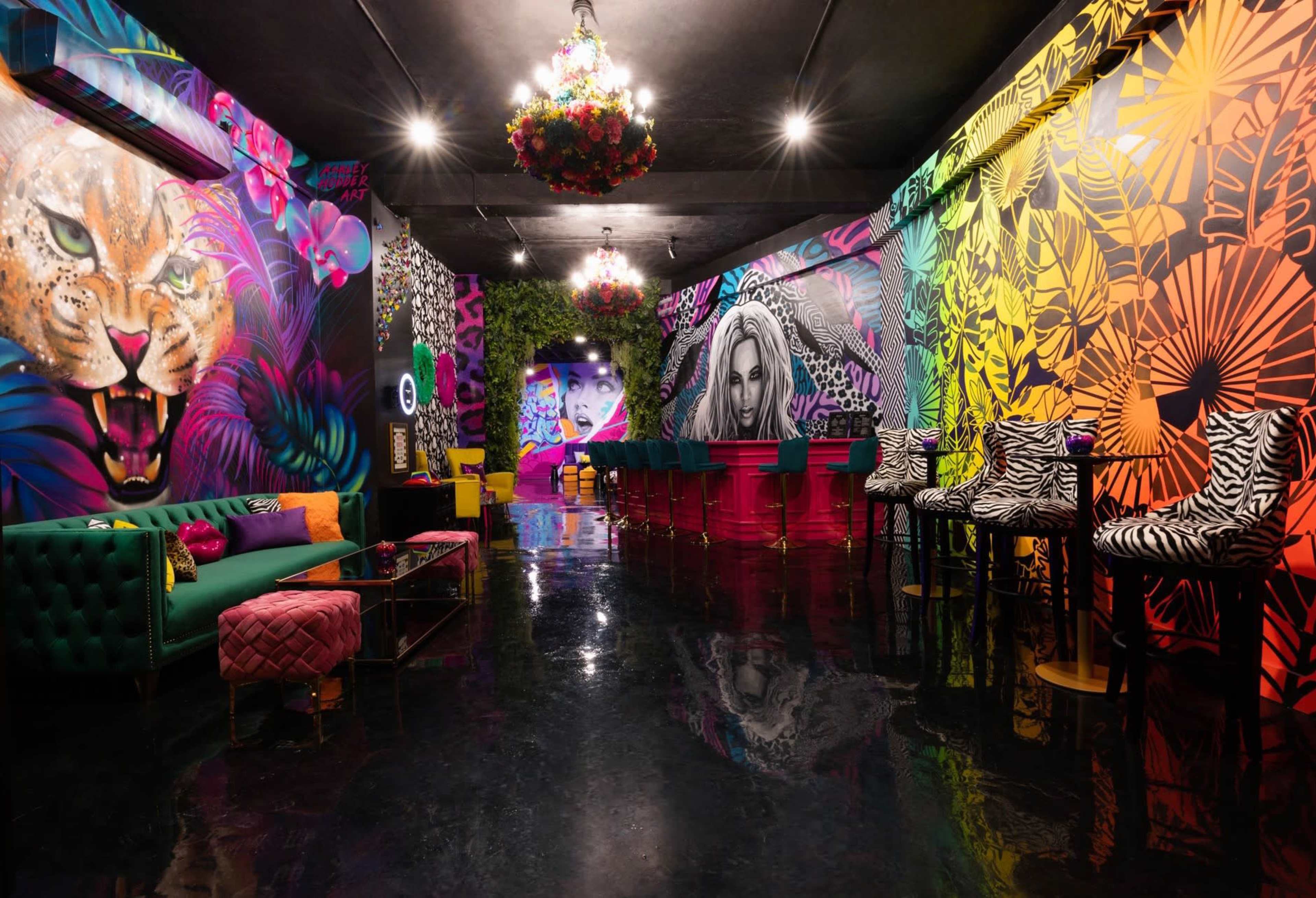 A vibrant lounge with bold, colorful murals of a lion and a woman's face, surrounded by stylish seating and a shiny black floor.