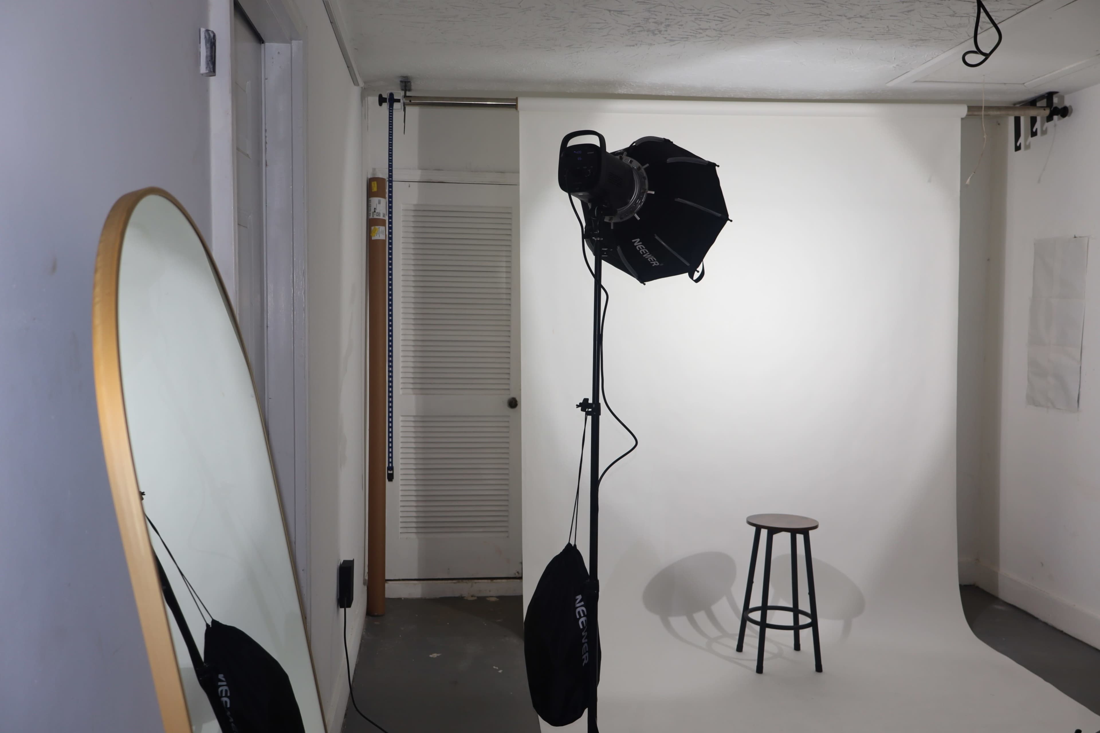 A photography studio setup with a mirror, a stool, and lighting equipment in front of a white backdrop.