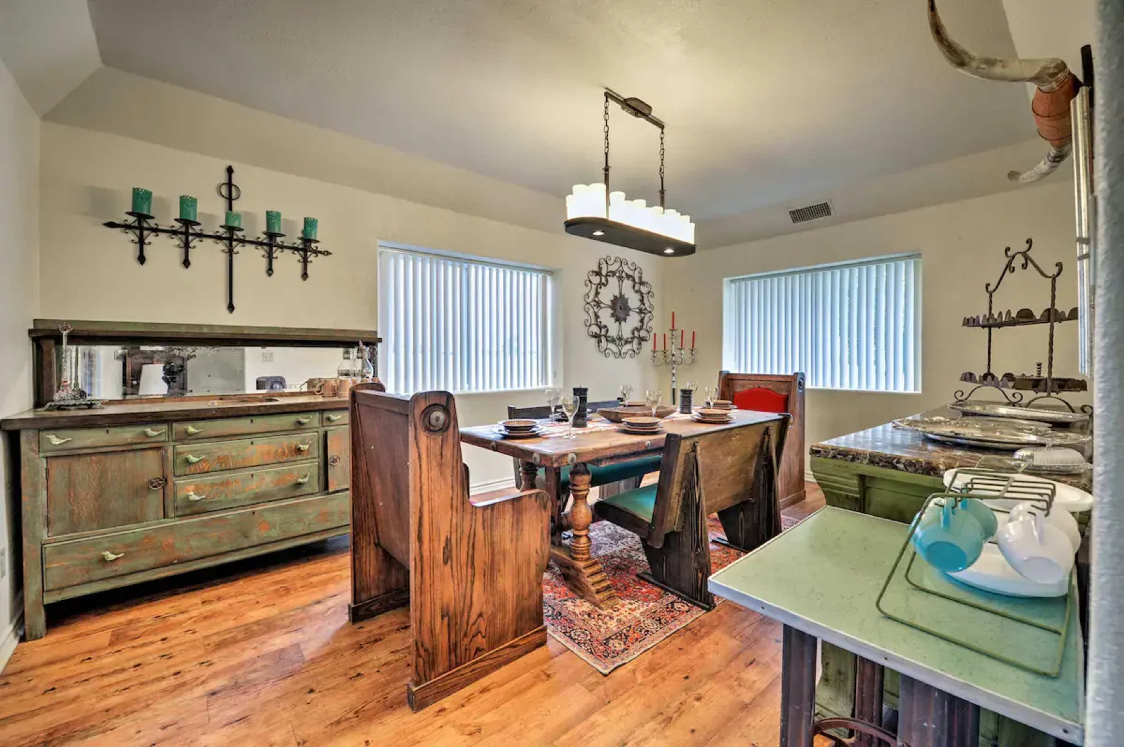 A well-furnished dining room featuring a wooden table, several chairs, and a sideboard, all complemented by large windows and decorative elements on the walls.
