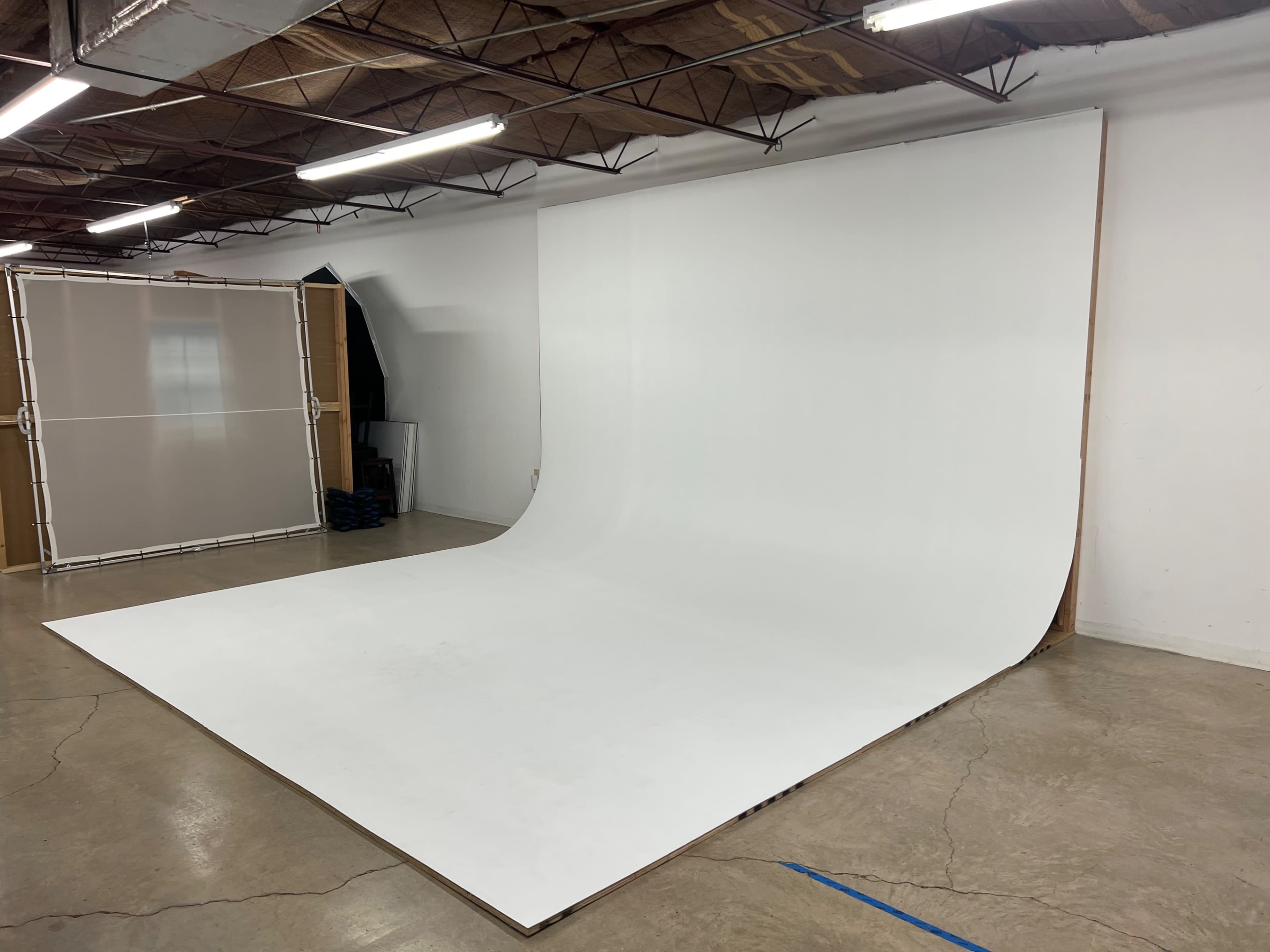 A spacious photography studio with a large, seamless white backdrop and polished concrete floors.