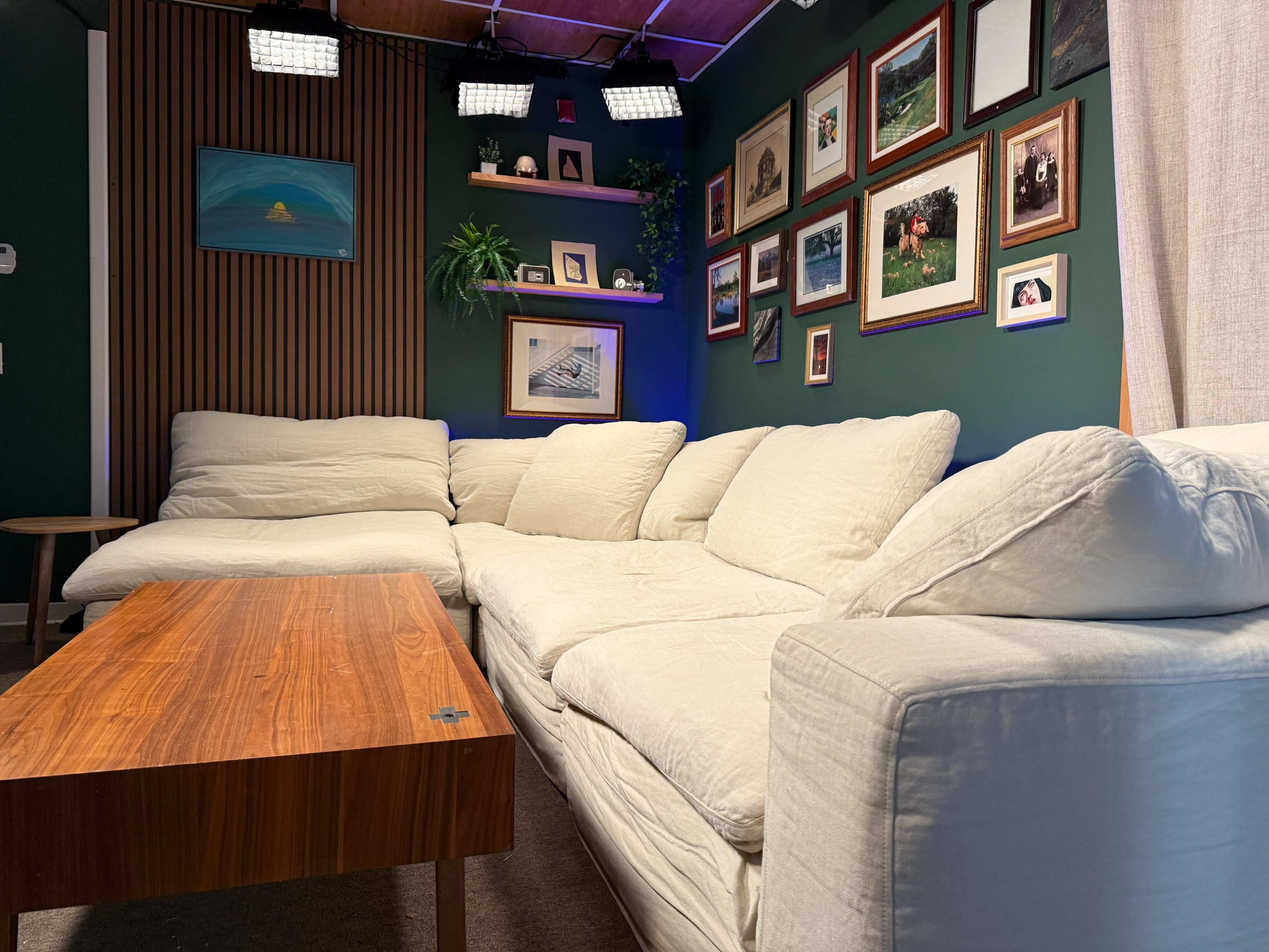 The image shows a cozy living room featuring a white sectional sofa, a wooden coffee table, and a wall adorned with framed photographs and artwork.