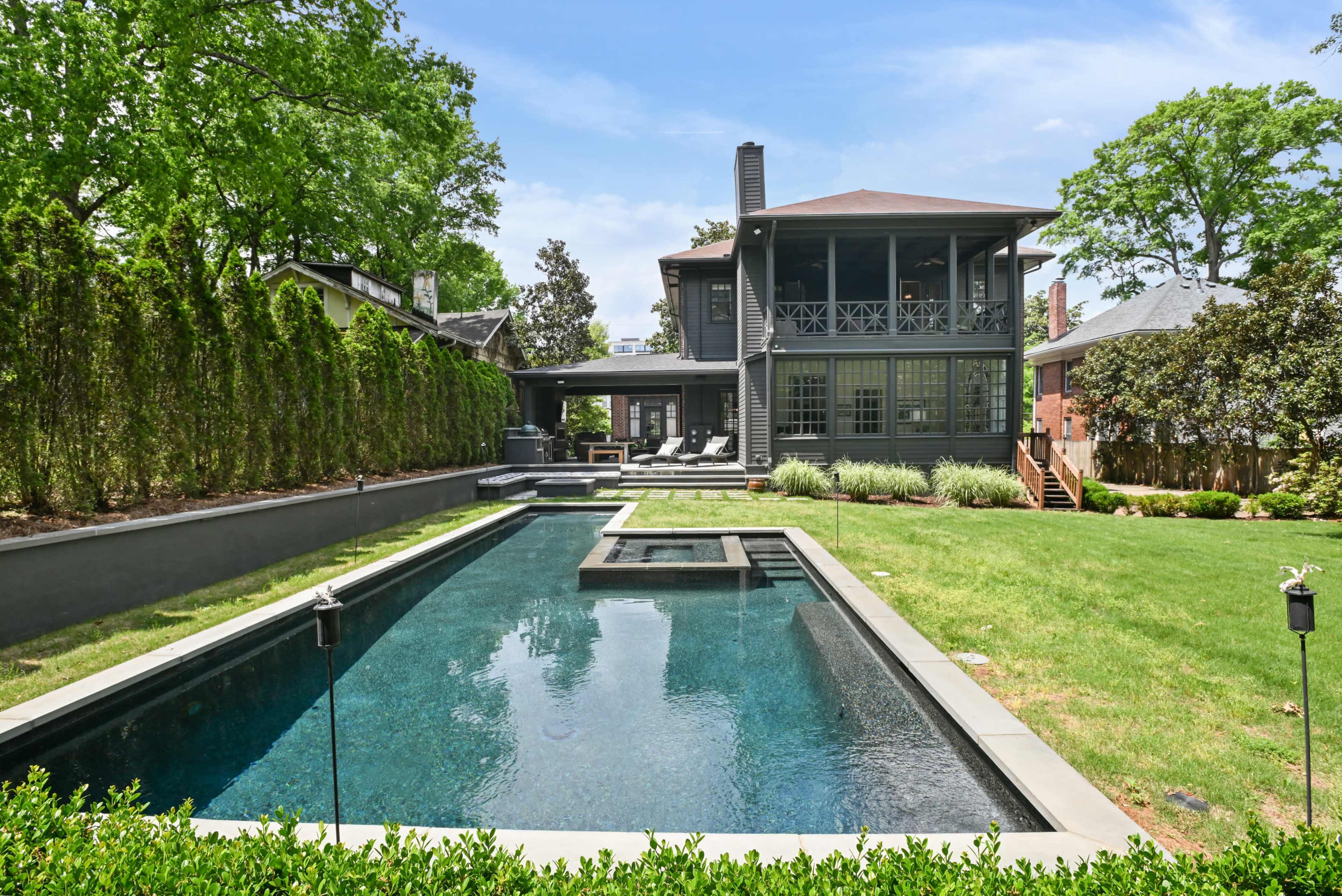 The image shows a modern house with a large backyard featuring a rectangular swimming pool and landscaped greenery.