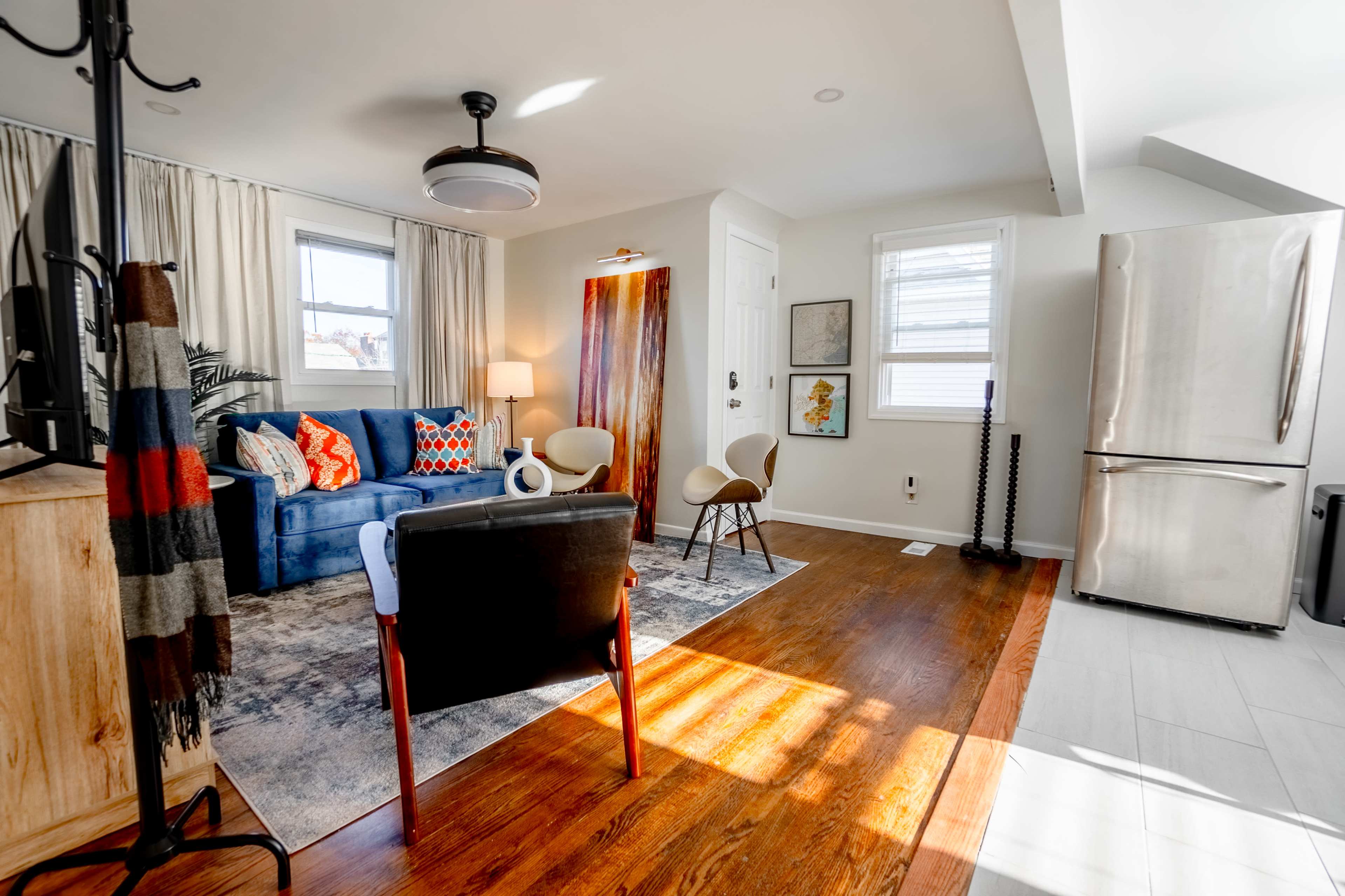A modern living room with a blue sofa, two chairs, a wooden coffee table, and a kitchen area featuring stainless steel appliances.