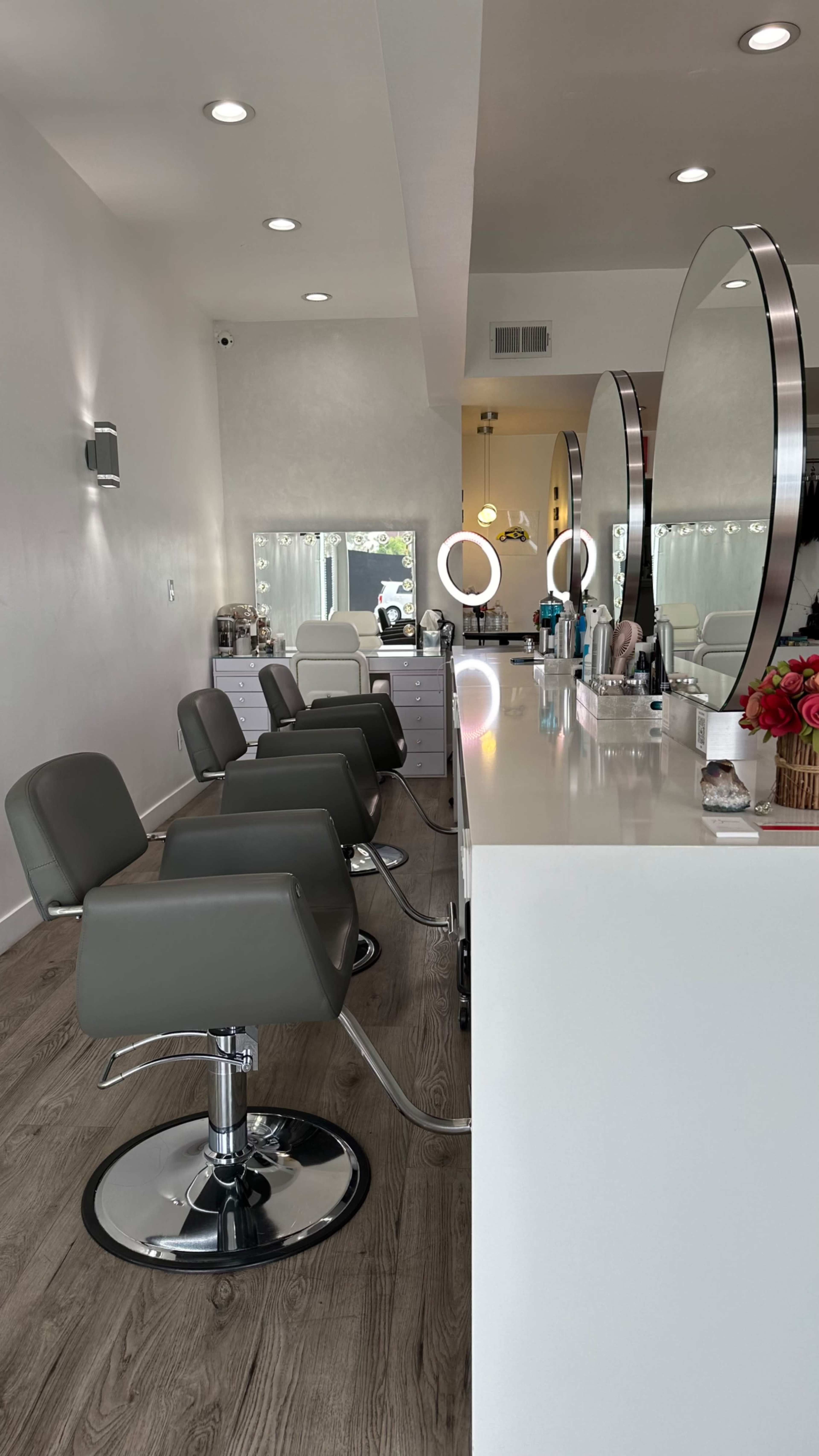 A modern hair salon with several gray salon chairs in front of a white countertop and large mirrors.
