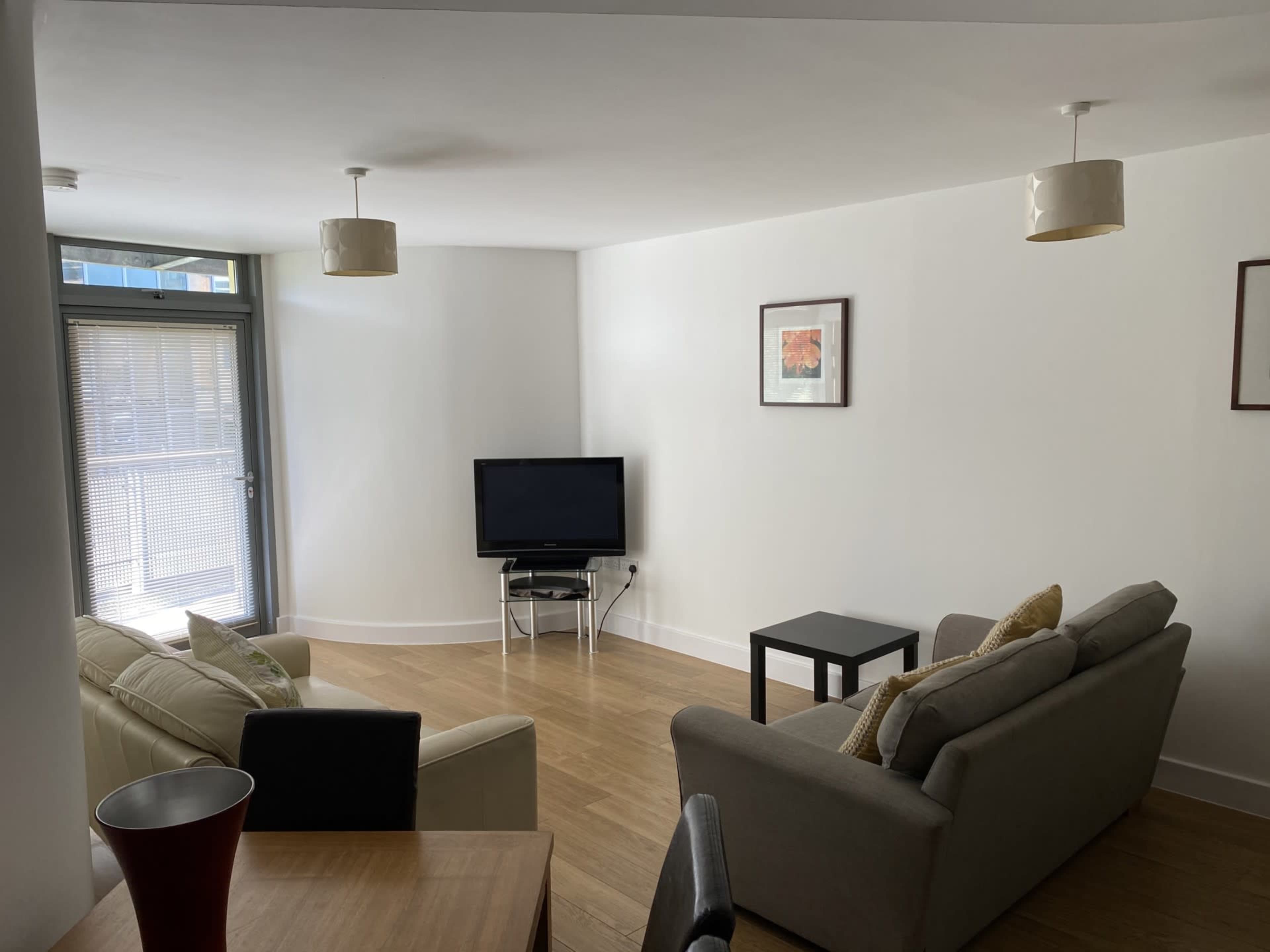 A modern, minimalist living room with two sofas, a coffee table, a television, and light-colored walls.