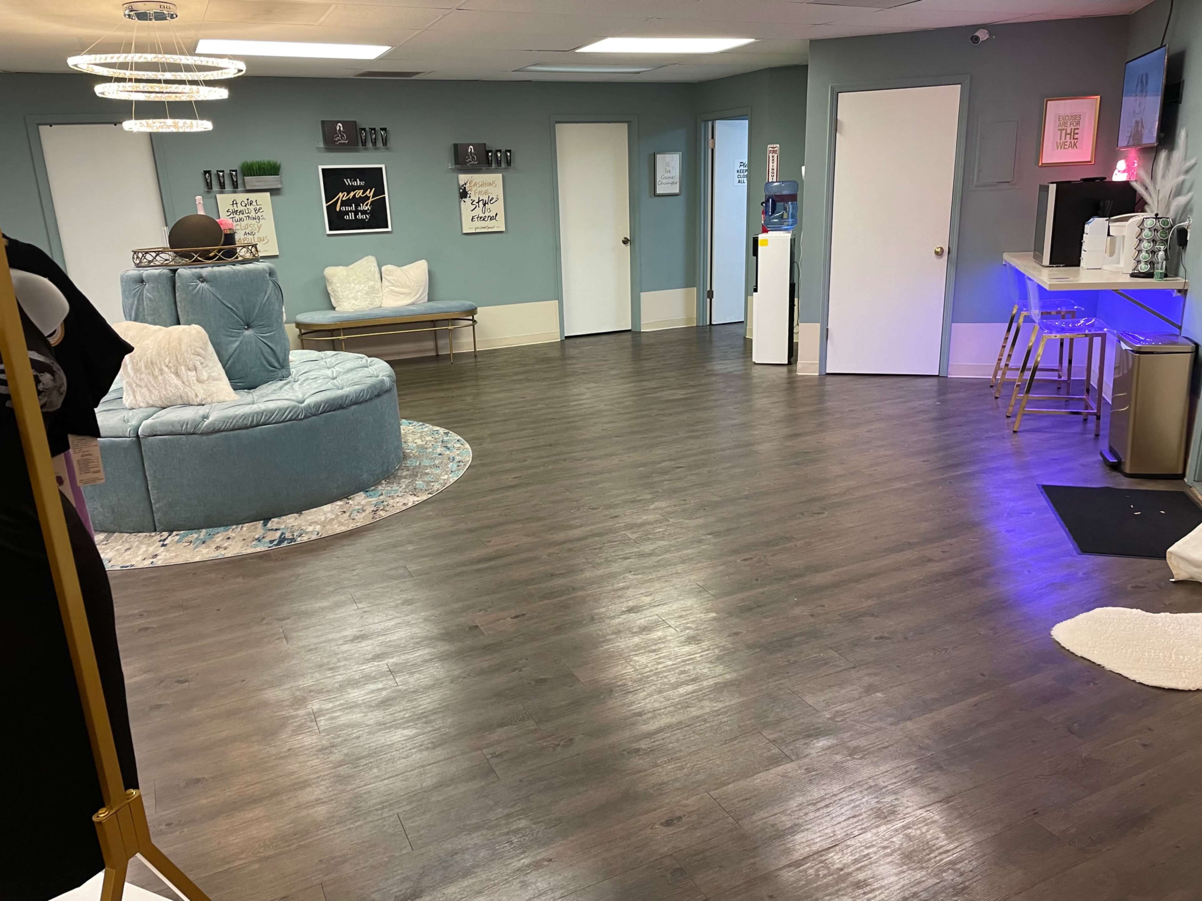 A spacious, well-lit room with light blue walls, a large circular sofa, and a bar area along one wall, featuring stools and decorative elements.