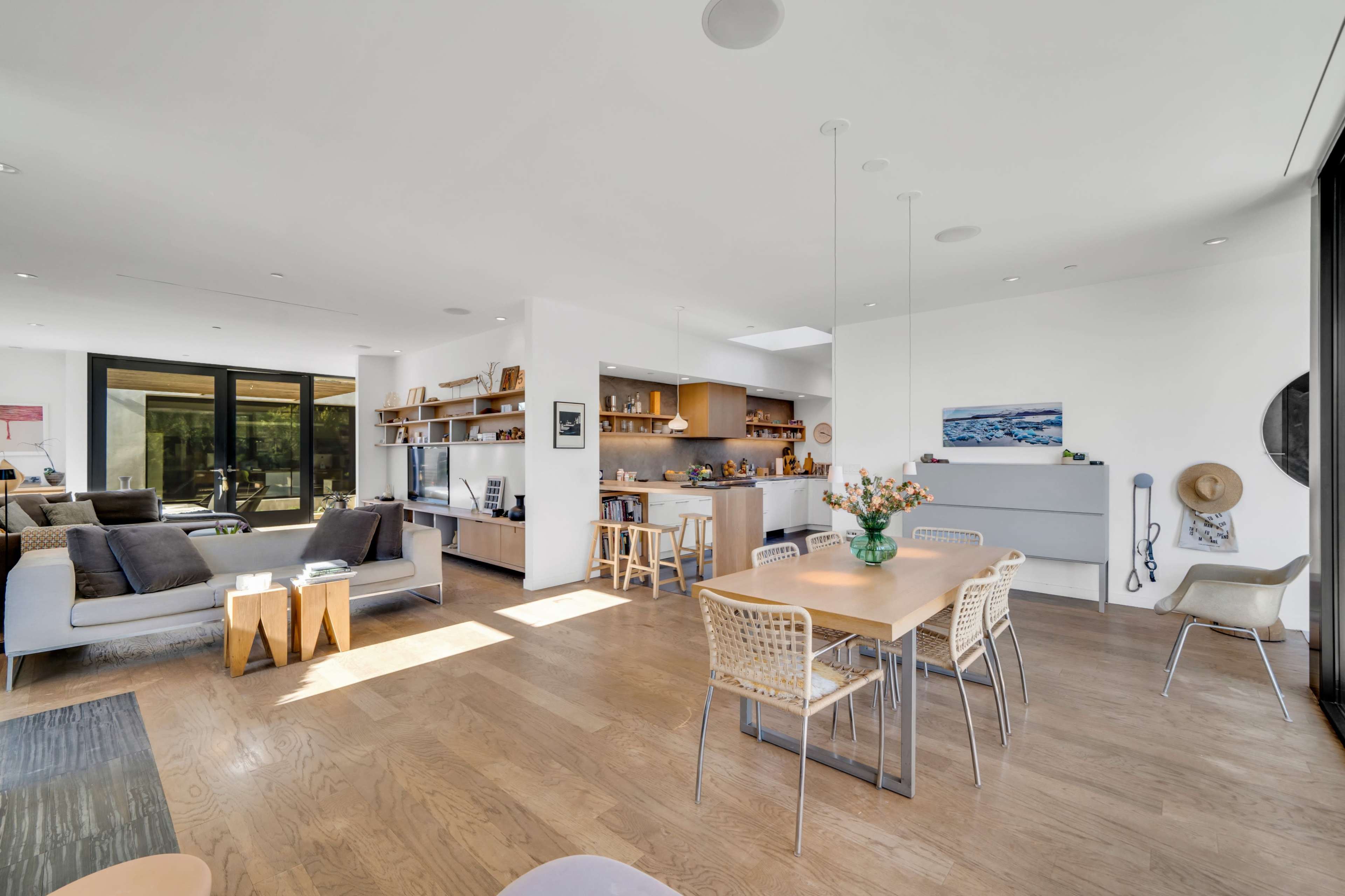 A modern open-concept living and dining area with light wooden floors, a spacious kitchen, and large windows allowing natural light.