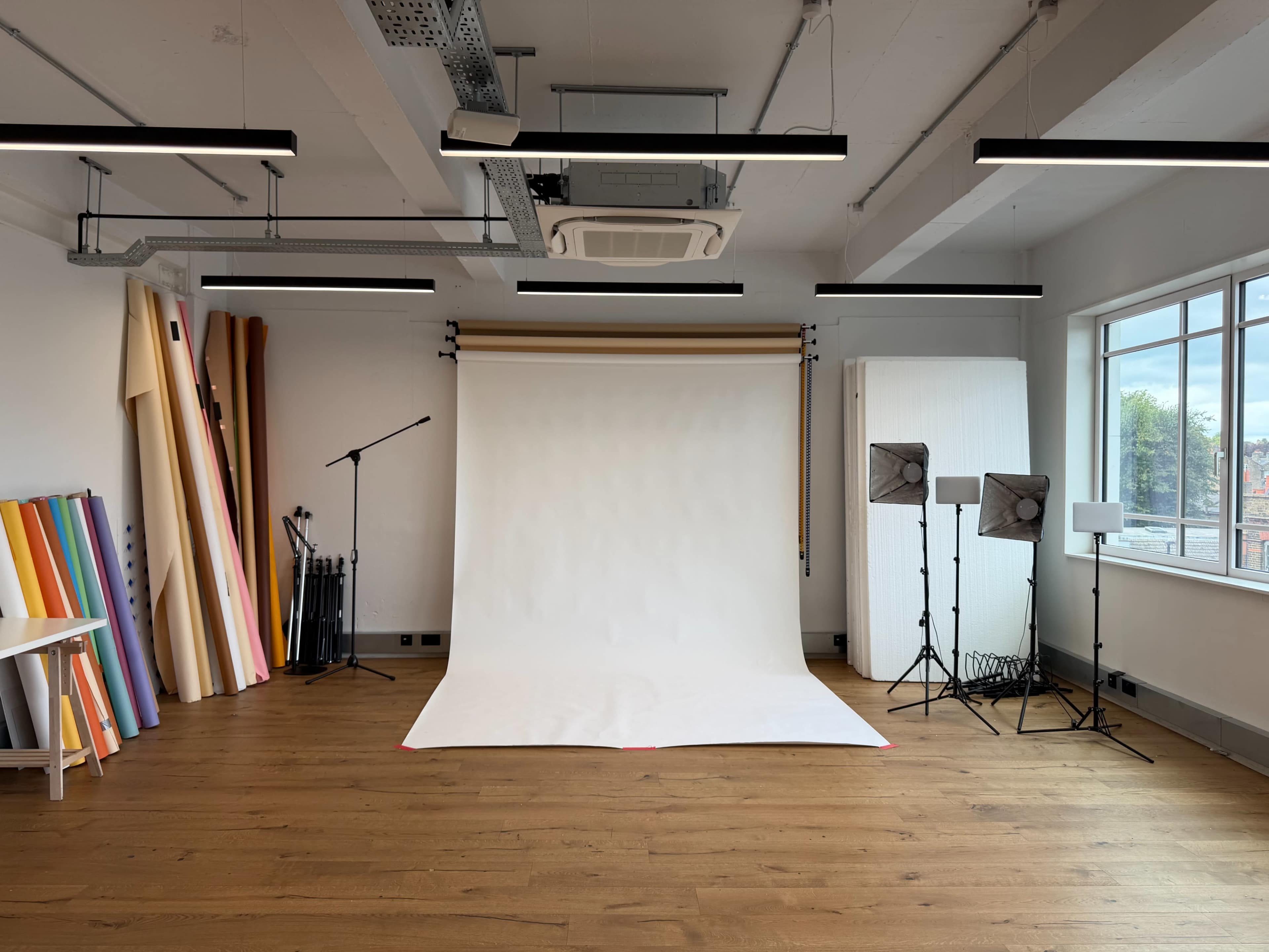 The image shows a spacious photography studio with a white backdrop, lighting equipment, and colorful rolls of photographic paper against the wall.