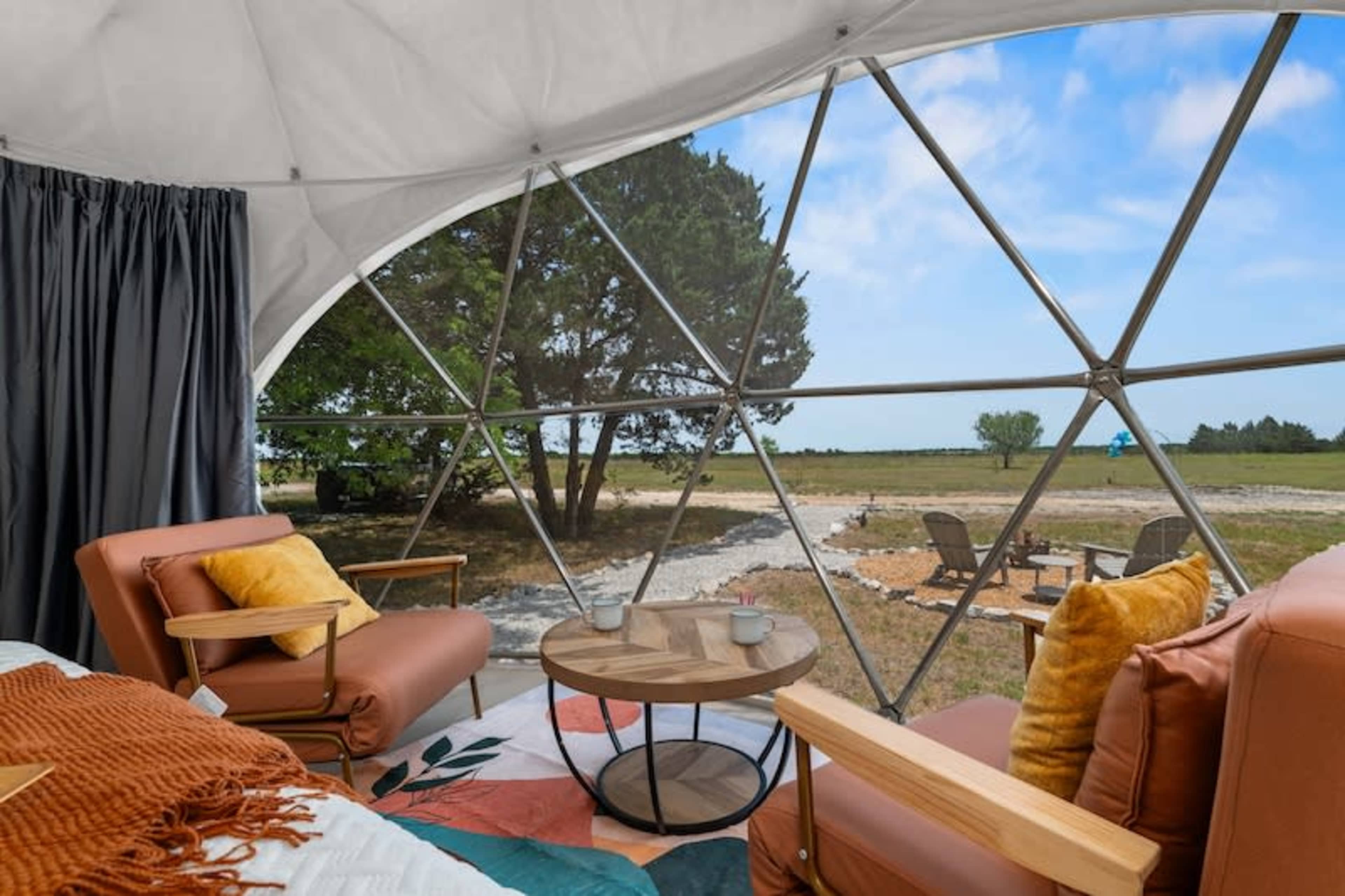 A geodesic dome interior features two chairs facing a large window with a view of an open landscape and seating area outside.