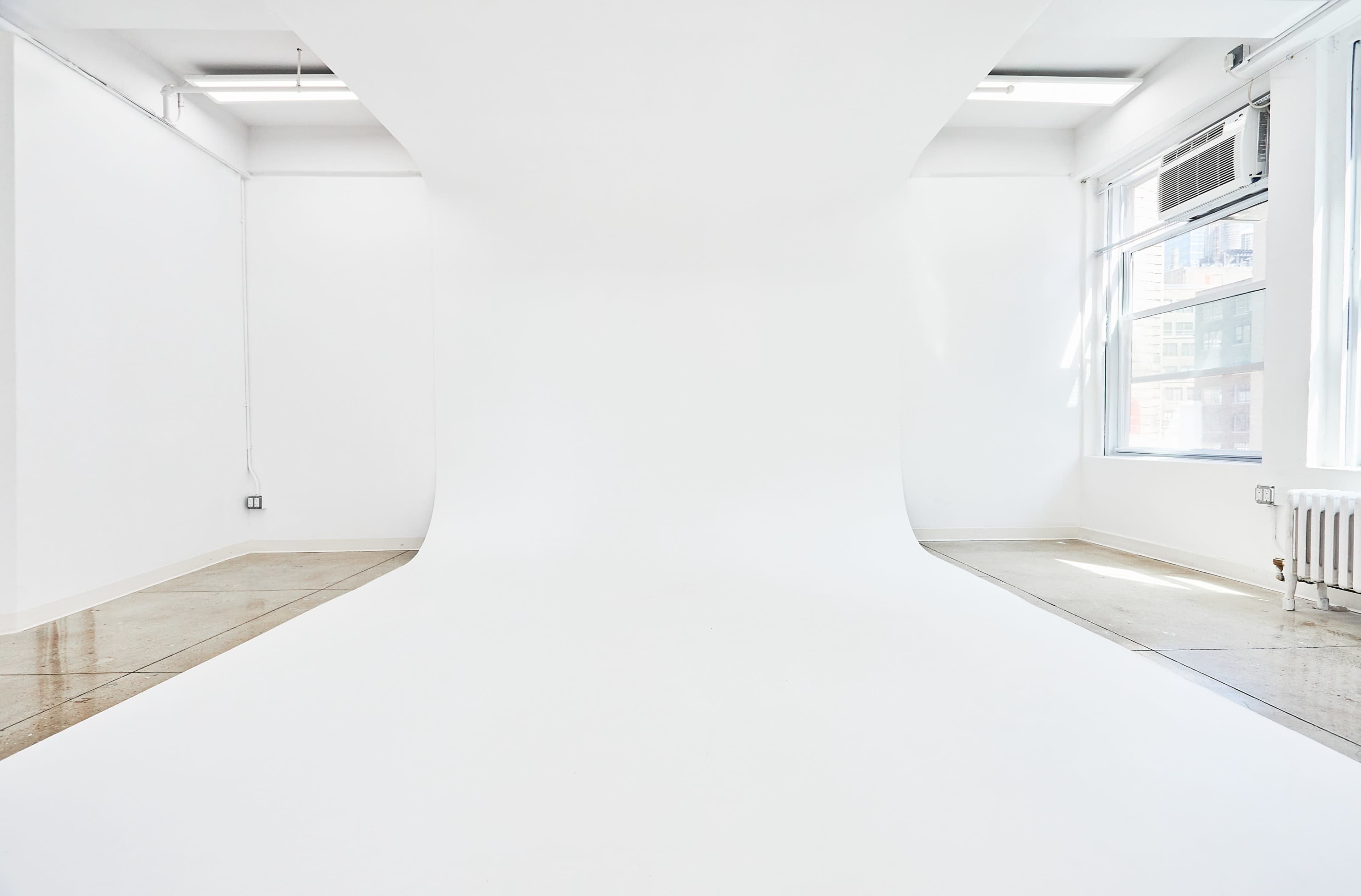 The image shows a minimalist photography studio with white walls and a seamless white backdrop.