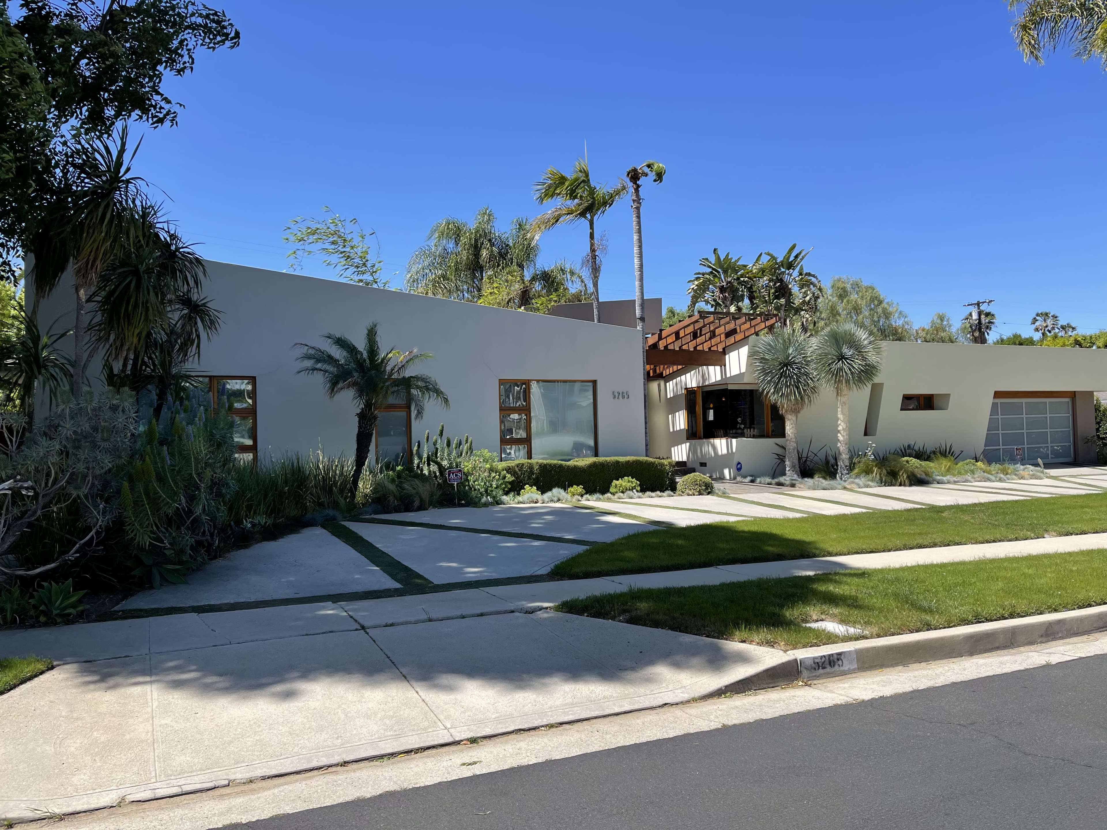 A modern house with a landscaped front yard, featuring palm trees and a driveway.