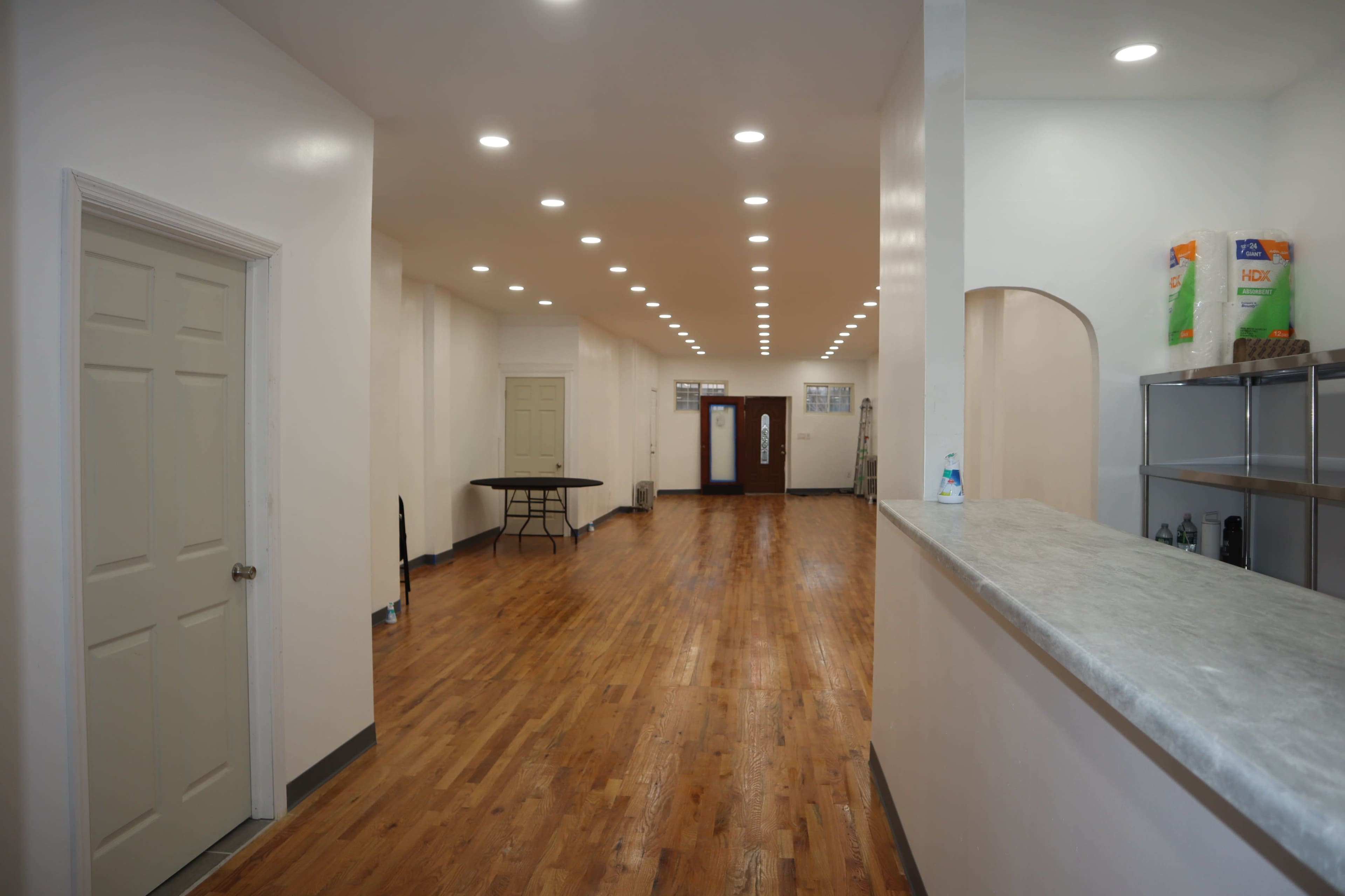 The interior of a spacious room features wooden flooring, white walls, and a reception area with a counter, alongside several doors leading to different sections.