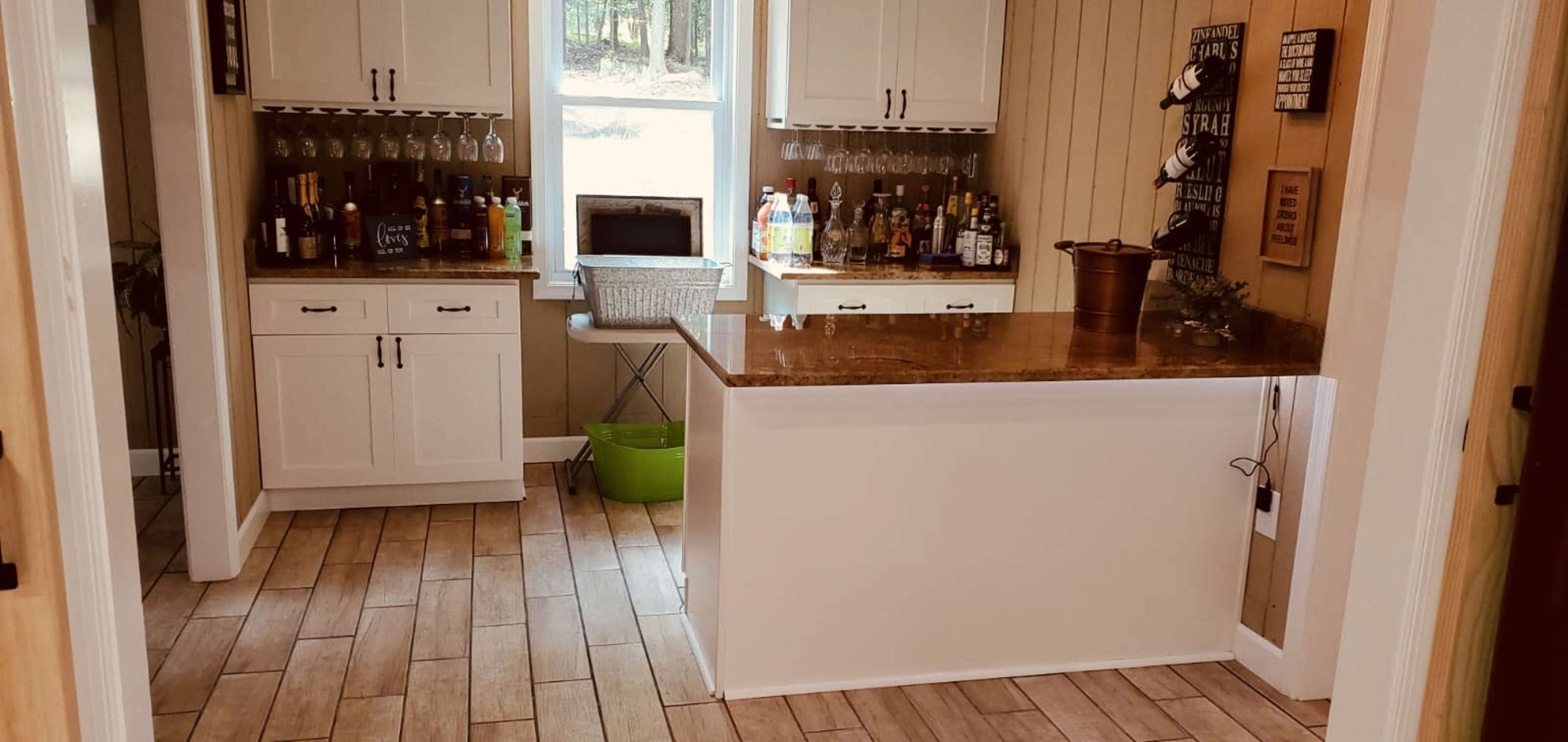 A home bar area with a central island and cabinets, surrounded by various bottles and glassware.