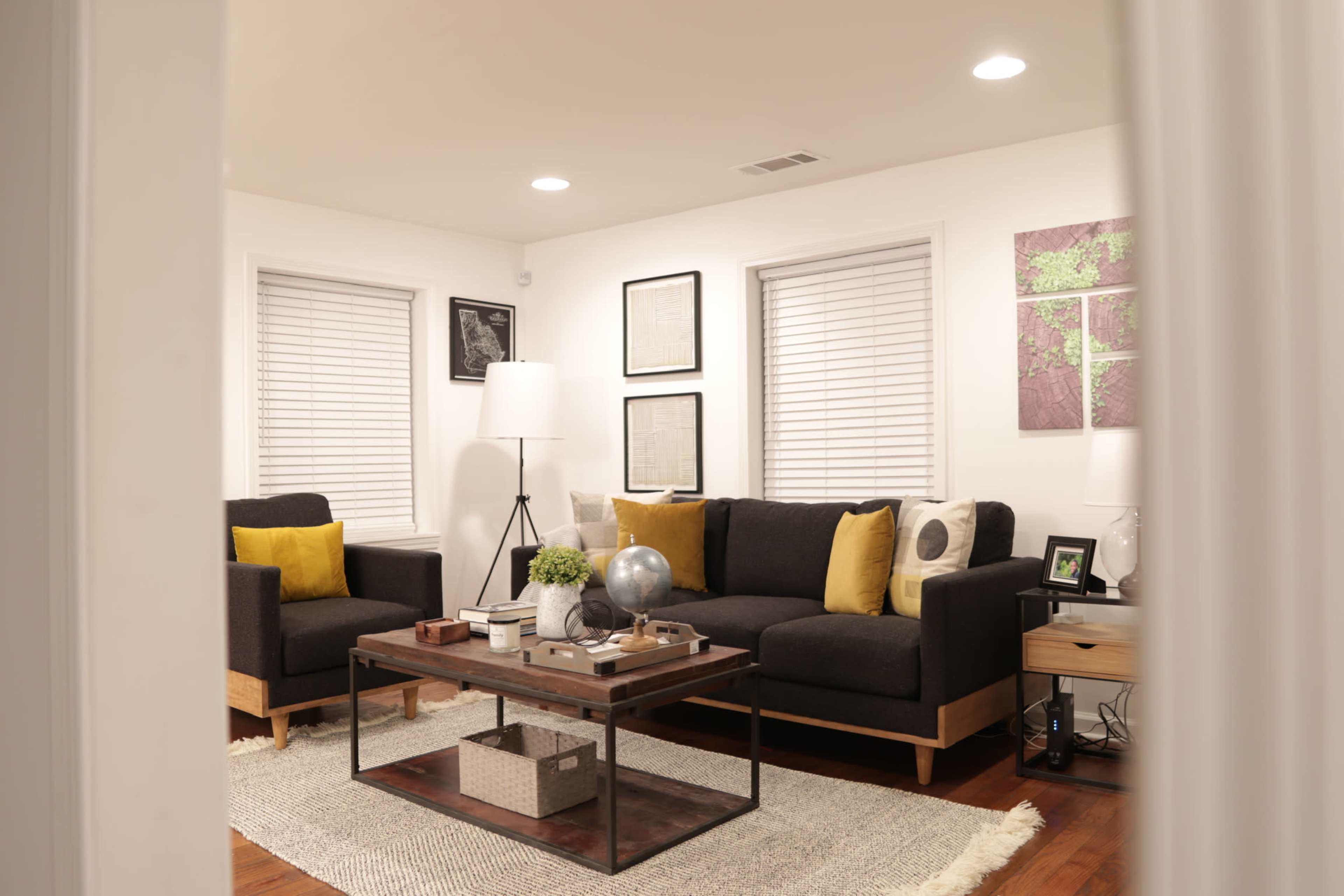 A modern living room features a sectional sofa and armchair with yellow cushions, a wooden coffee table, and framed artwork on the walls.