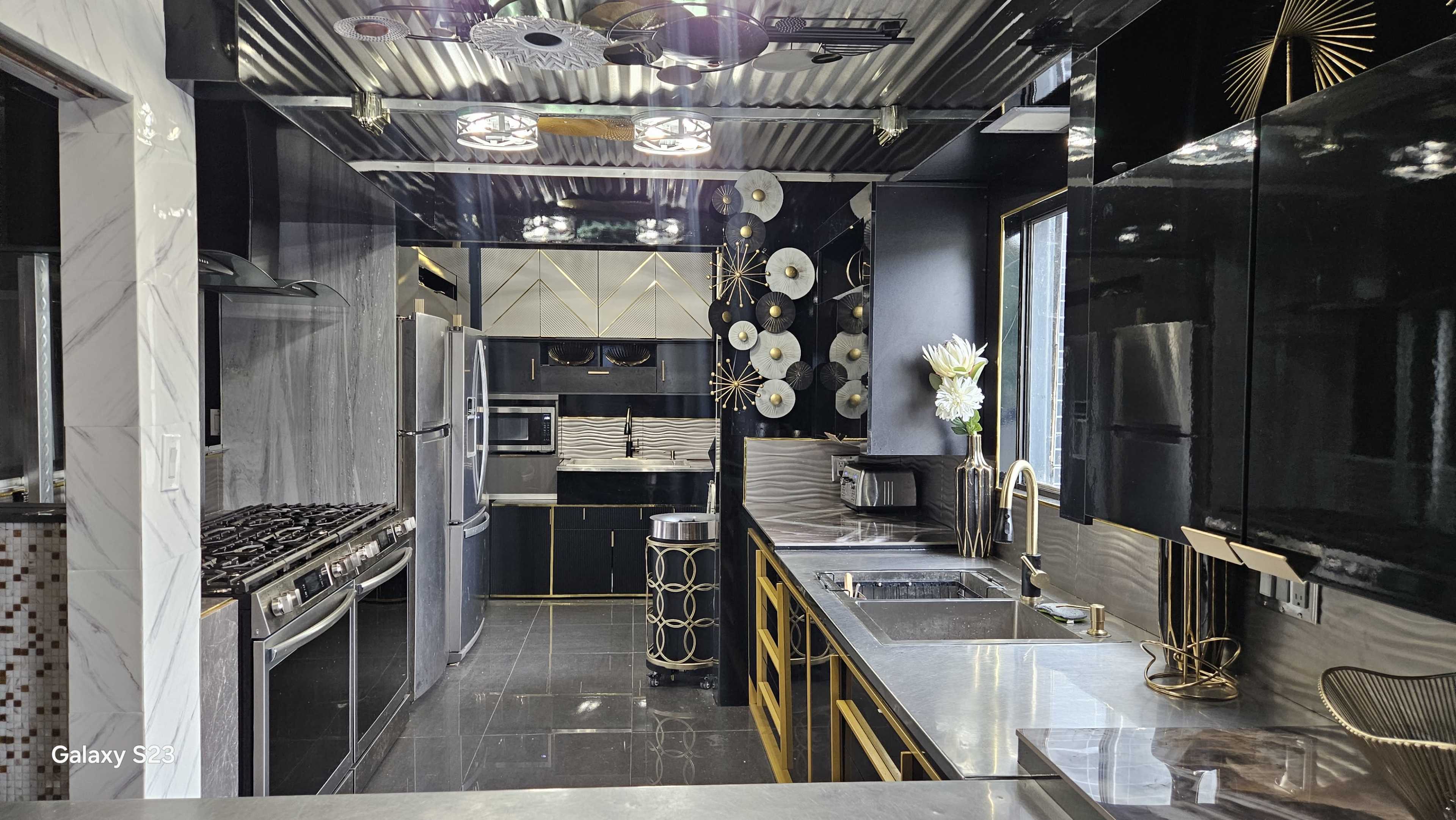 The image shows a modern kitchen with sleek black cabinetry, stainless steel appliances, and a contrasting gold and white decorative scheme.