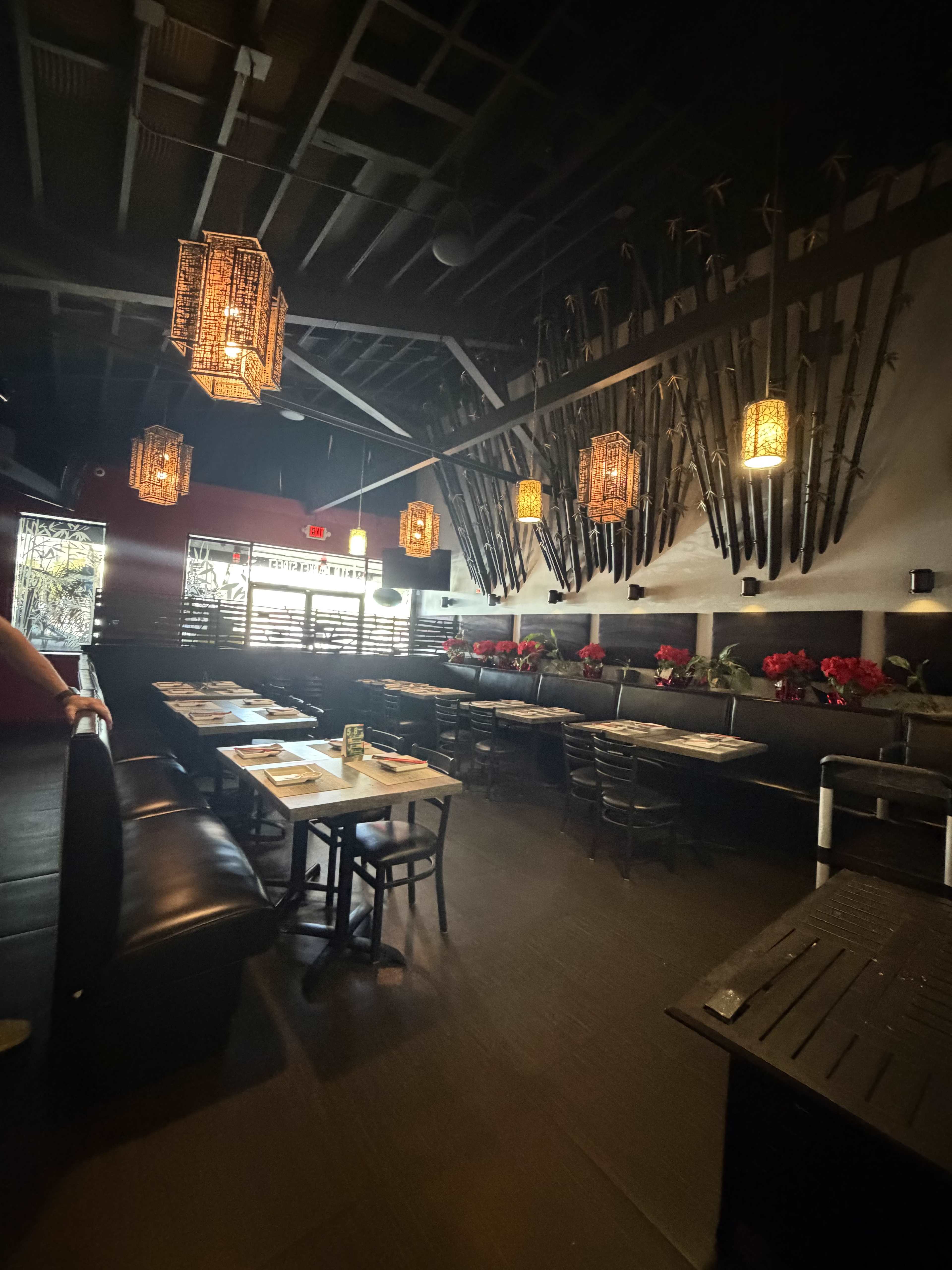 The image shows the interior of a dimly lit restaurant featuring bamboo decor, hanging lanterns, and tables set for dining.