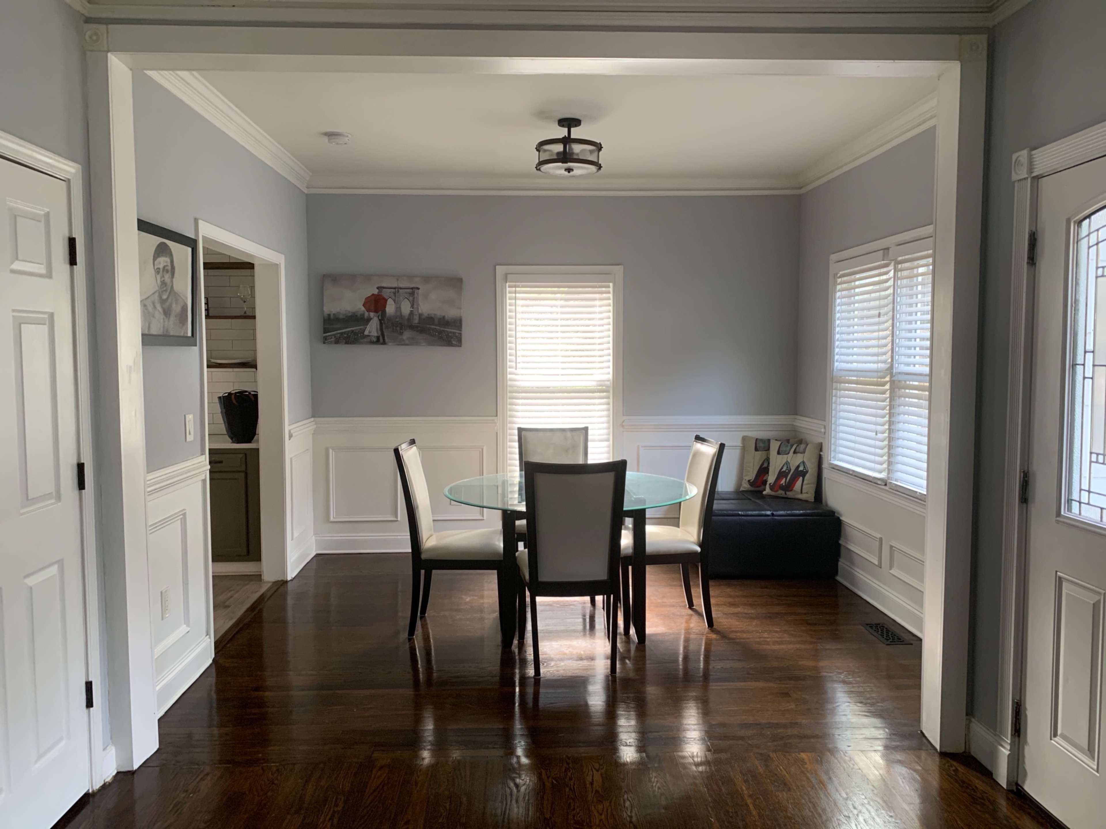 A dining area with a glass table surrounded by four chairs, set against a light blue wall and framed by decorative molding.
