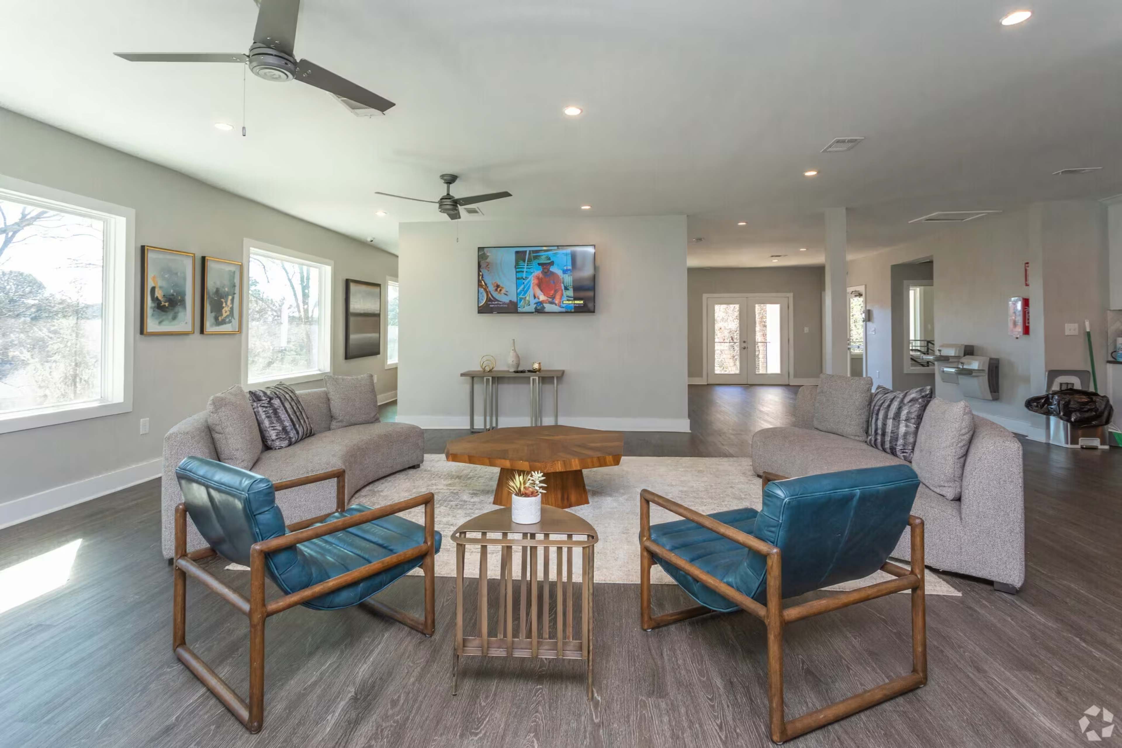 The image shows a modern living room with two sofas, two armchairs, a wooden coffee table, and a wall-mounted television.