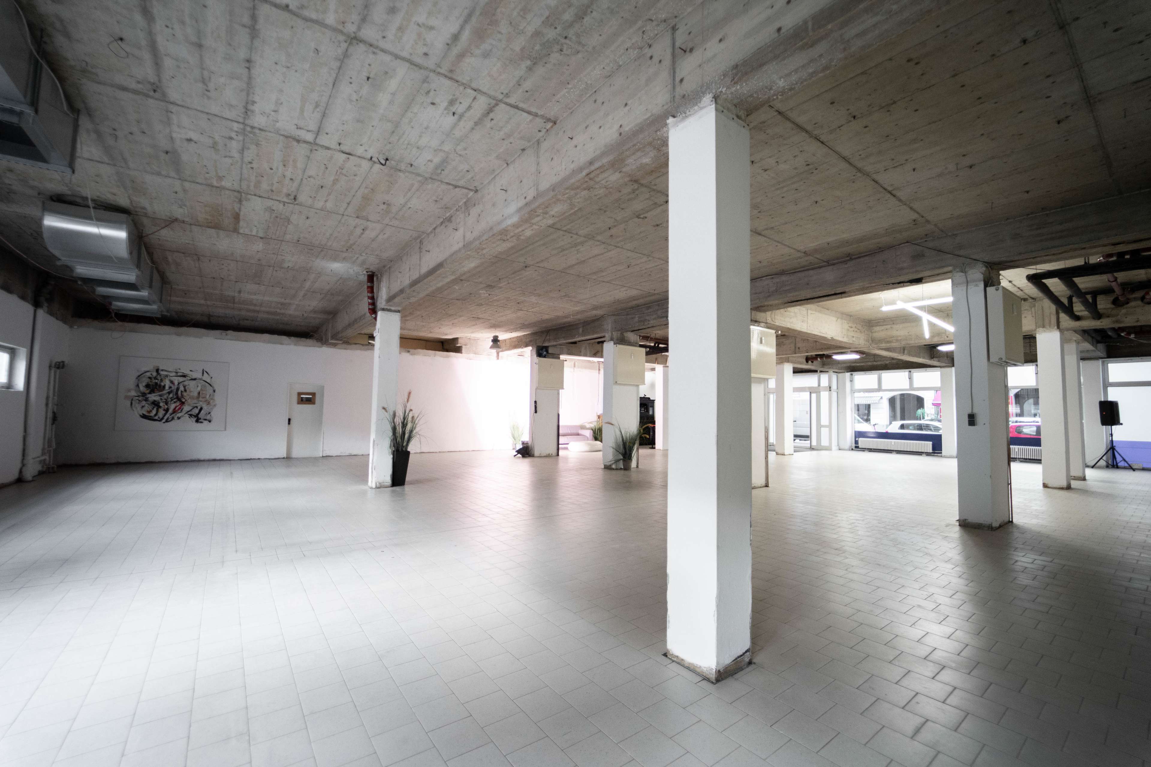 A spacious, empty industrial-style room with concrete ceilings and walls, featuring tiled flooring and several columns.
