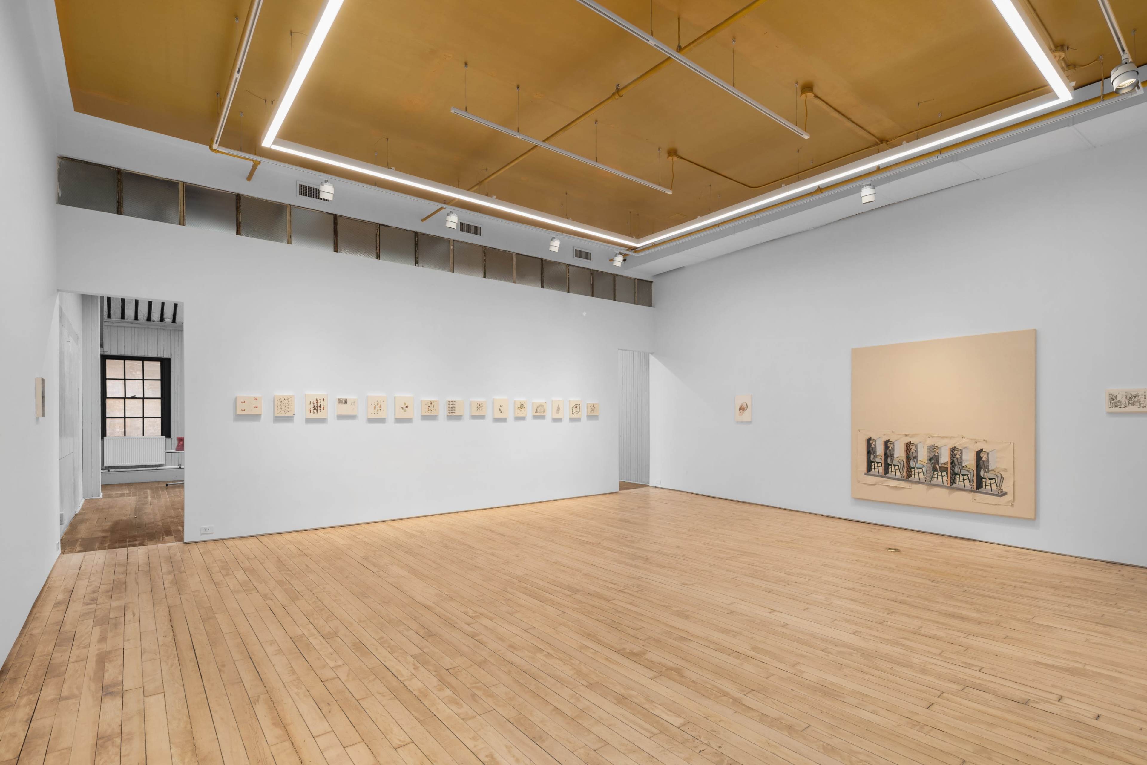 An art gallery with wooden floors and a series of framed artworks displayed on the walls under bright overhead lighting.