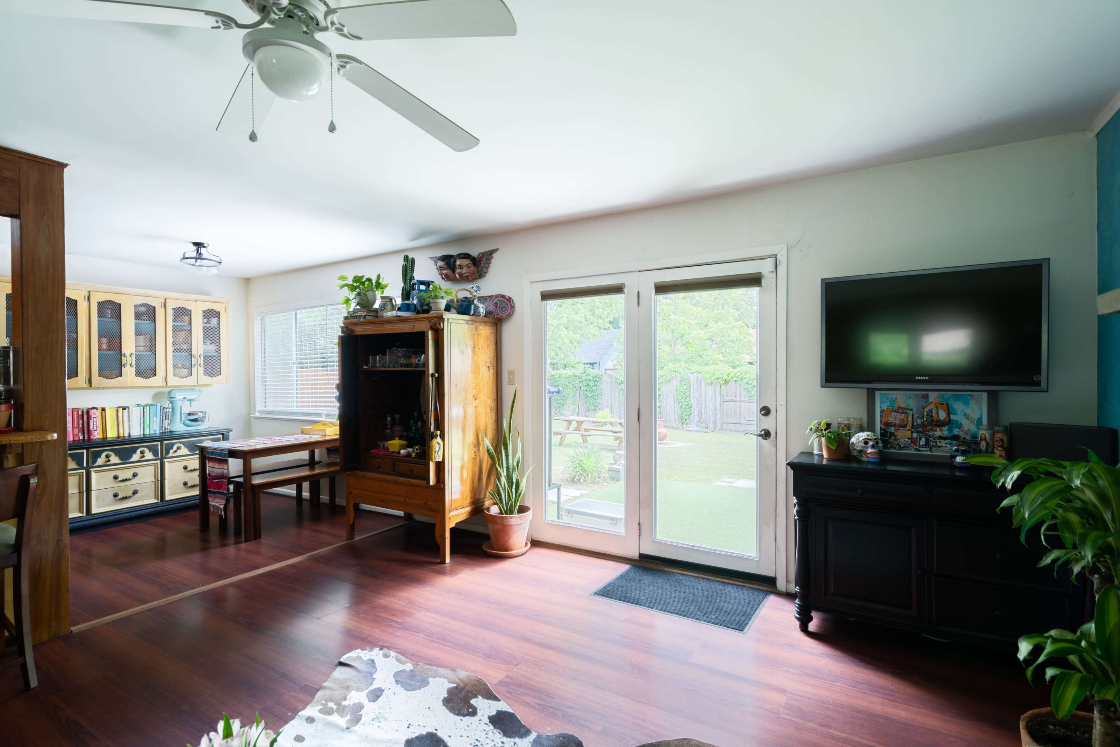 A bright living area features a wooden cabinet, table, and sliding glass door opening to a backyard.