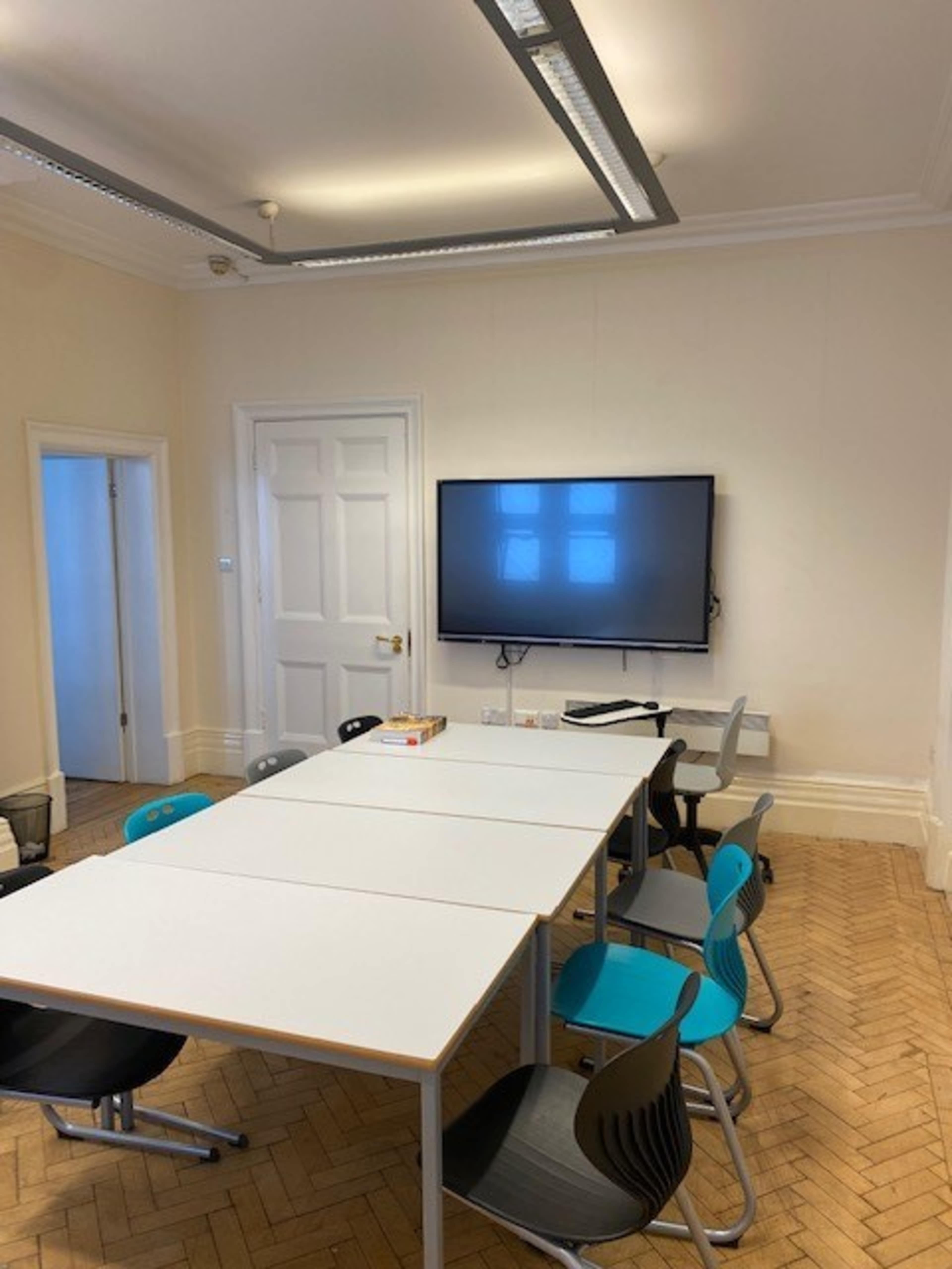 A modern conference room features a large table surrounded by colorful chairs and a wall-mounted television.