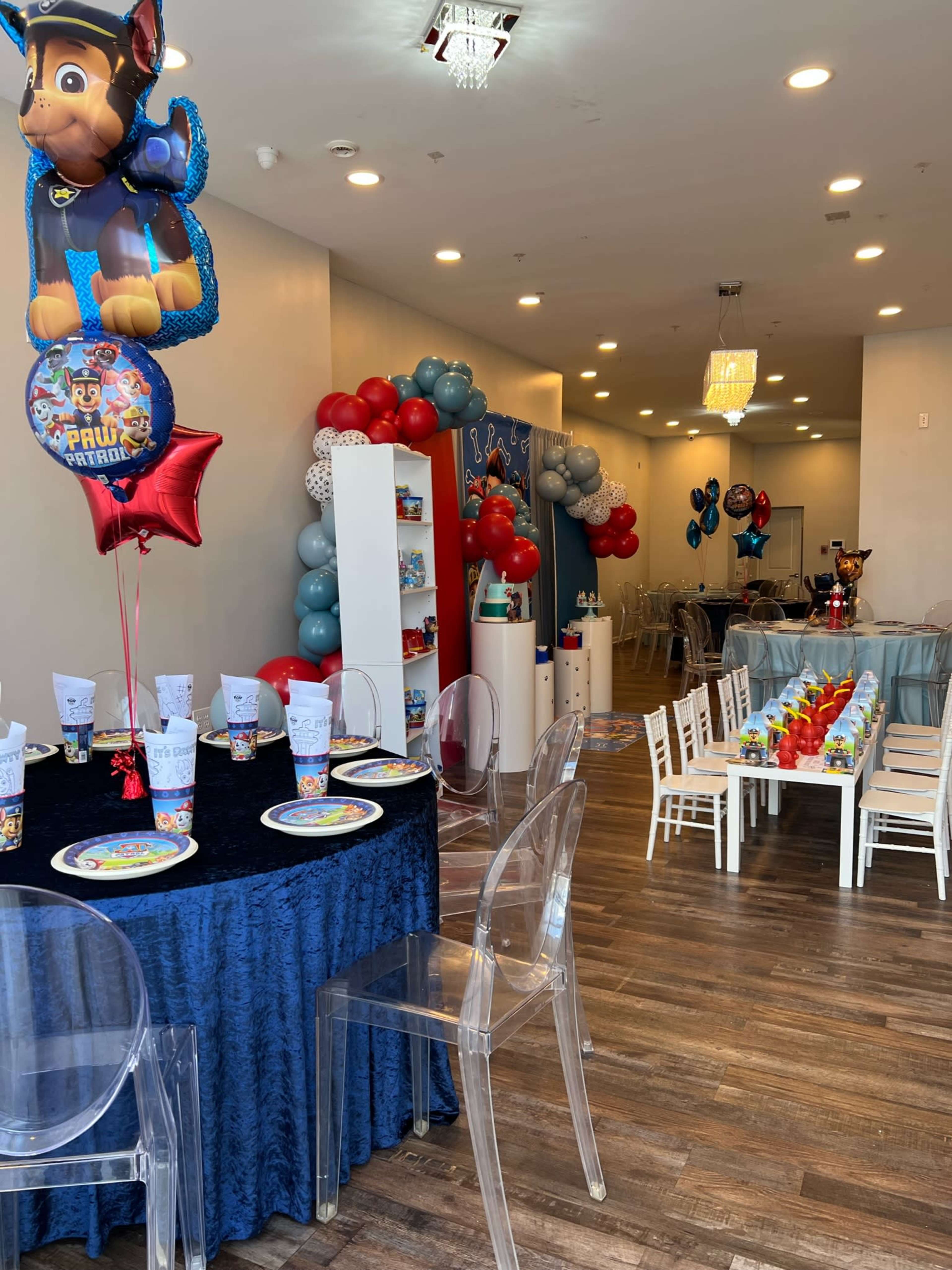 A brightly decorated party space with a table set for children's celebrations, featuring themed tableware and colorful balloons.