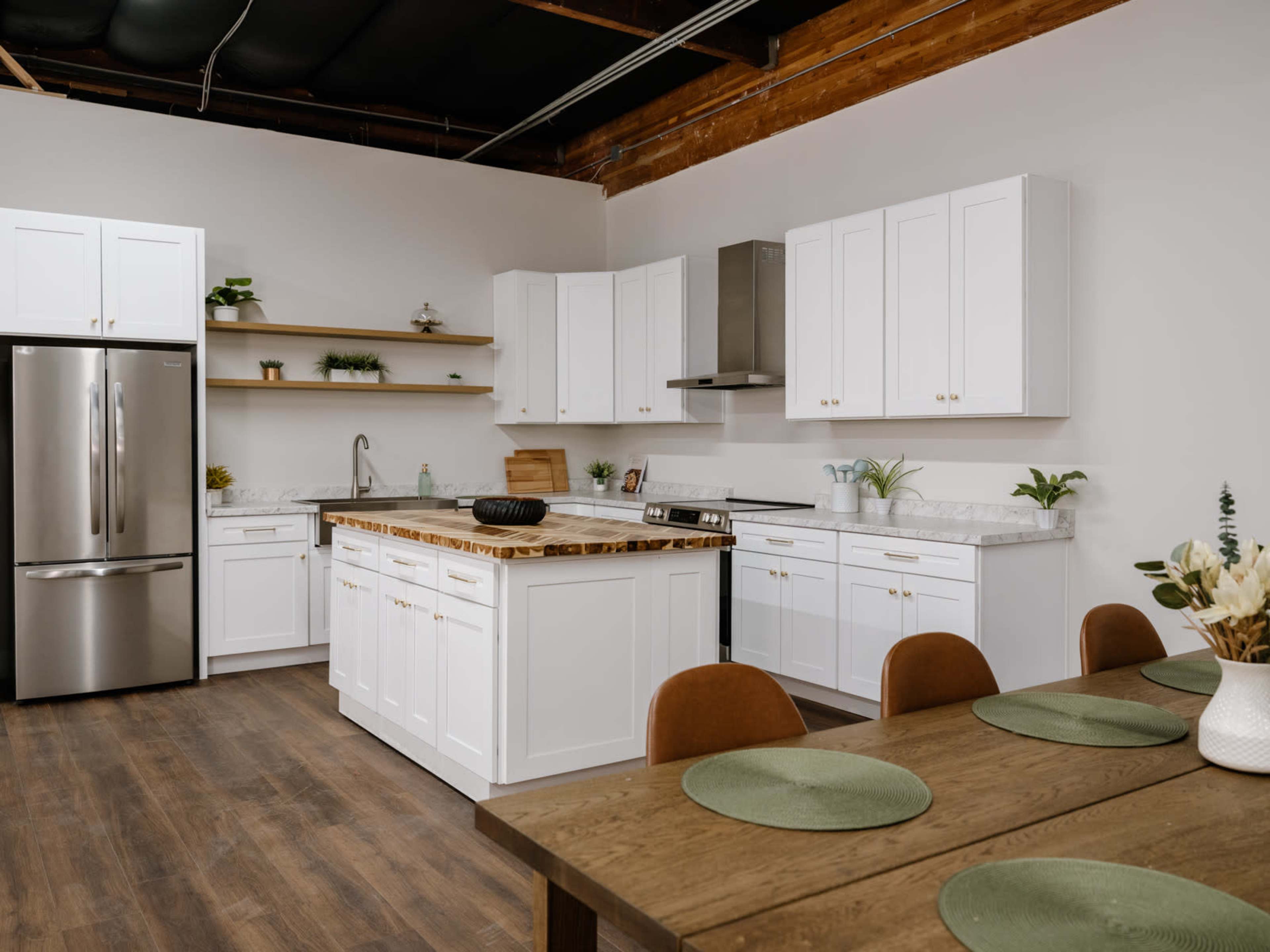 A modern kitchen features white cabinetry, a marble countertop, stainless steel appliances, and a dining table set with green place mats.