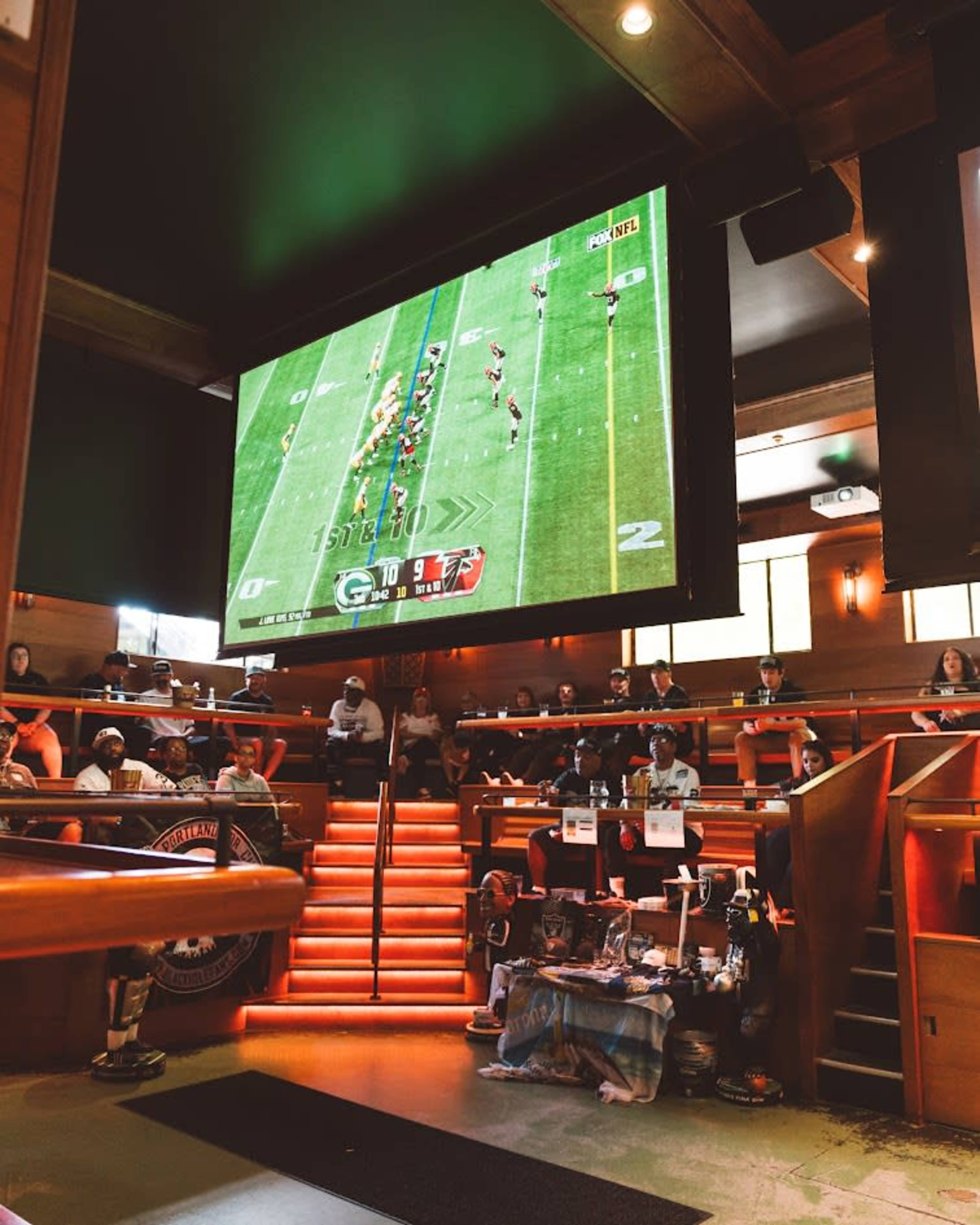 A large screen displays a football game in a lively sports bar with patrons seated around the venue.