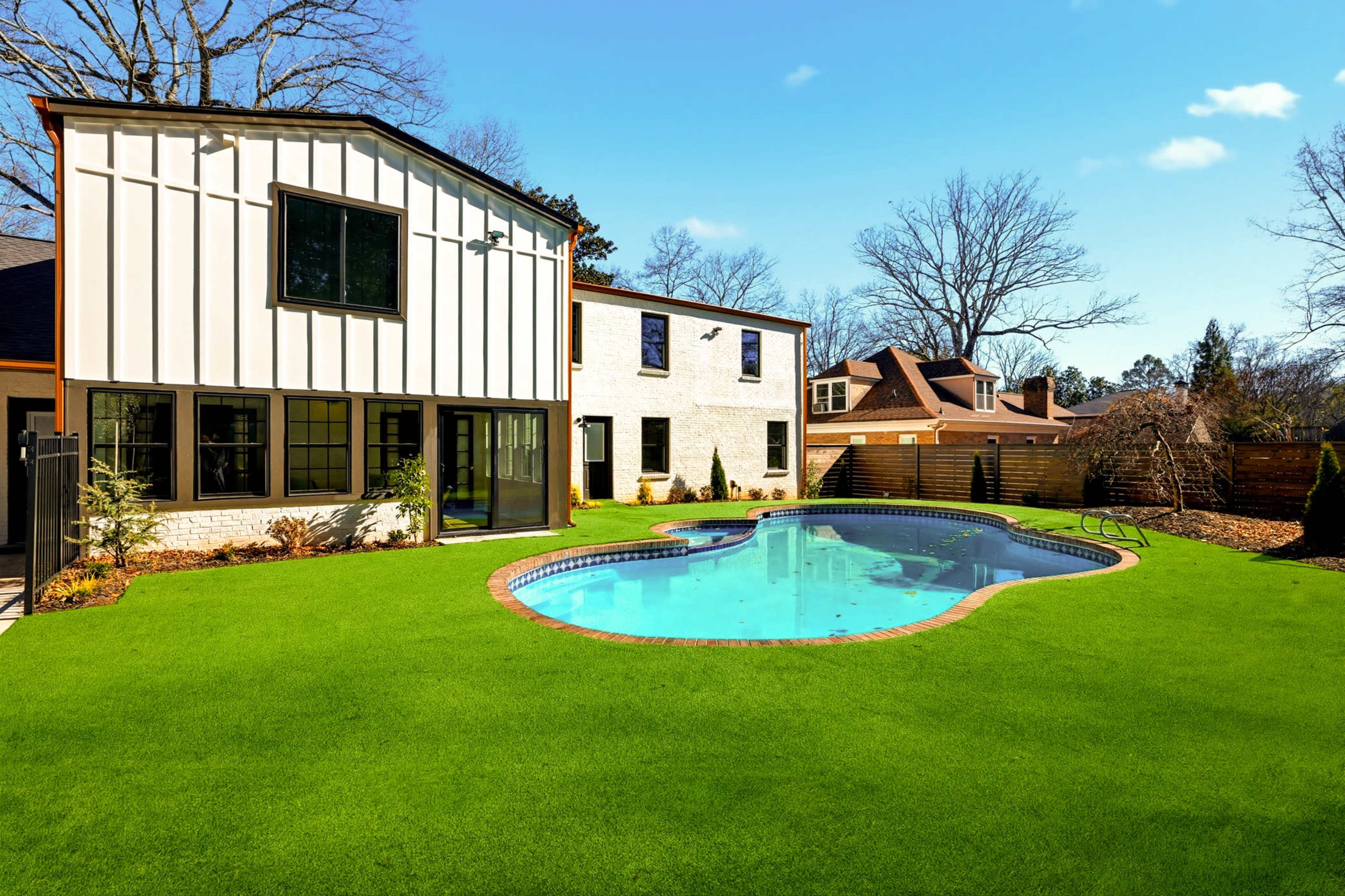 A modern house features a swimming pool surrounded by artificial turf and landscaped yard.