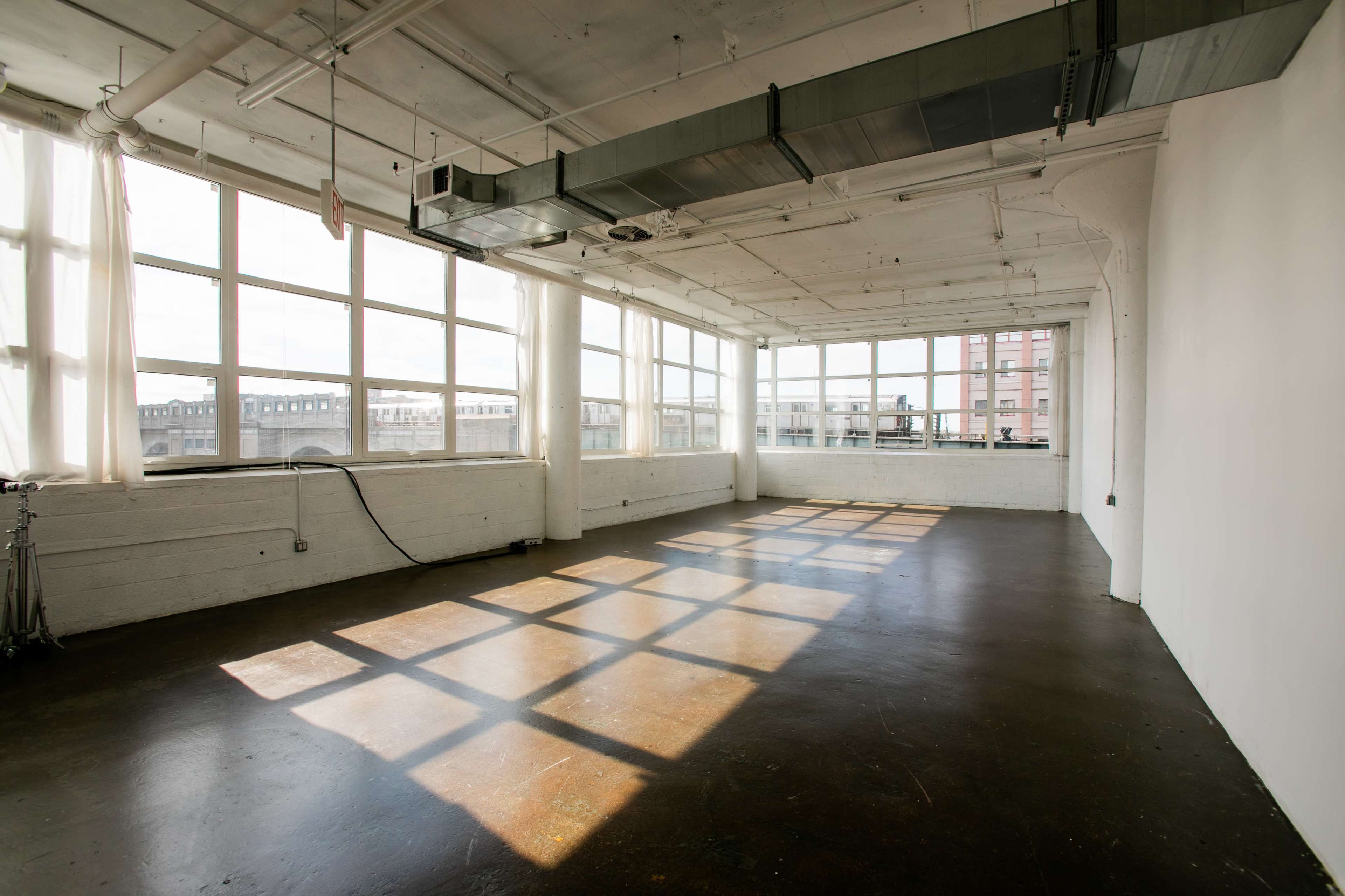 A spacious, empty room with large windows allowing sunlight to create shadows on a polished concrete floor.
