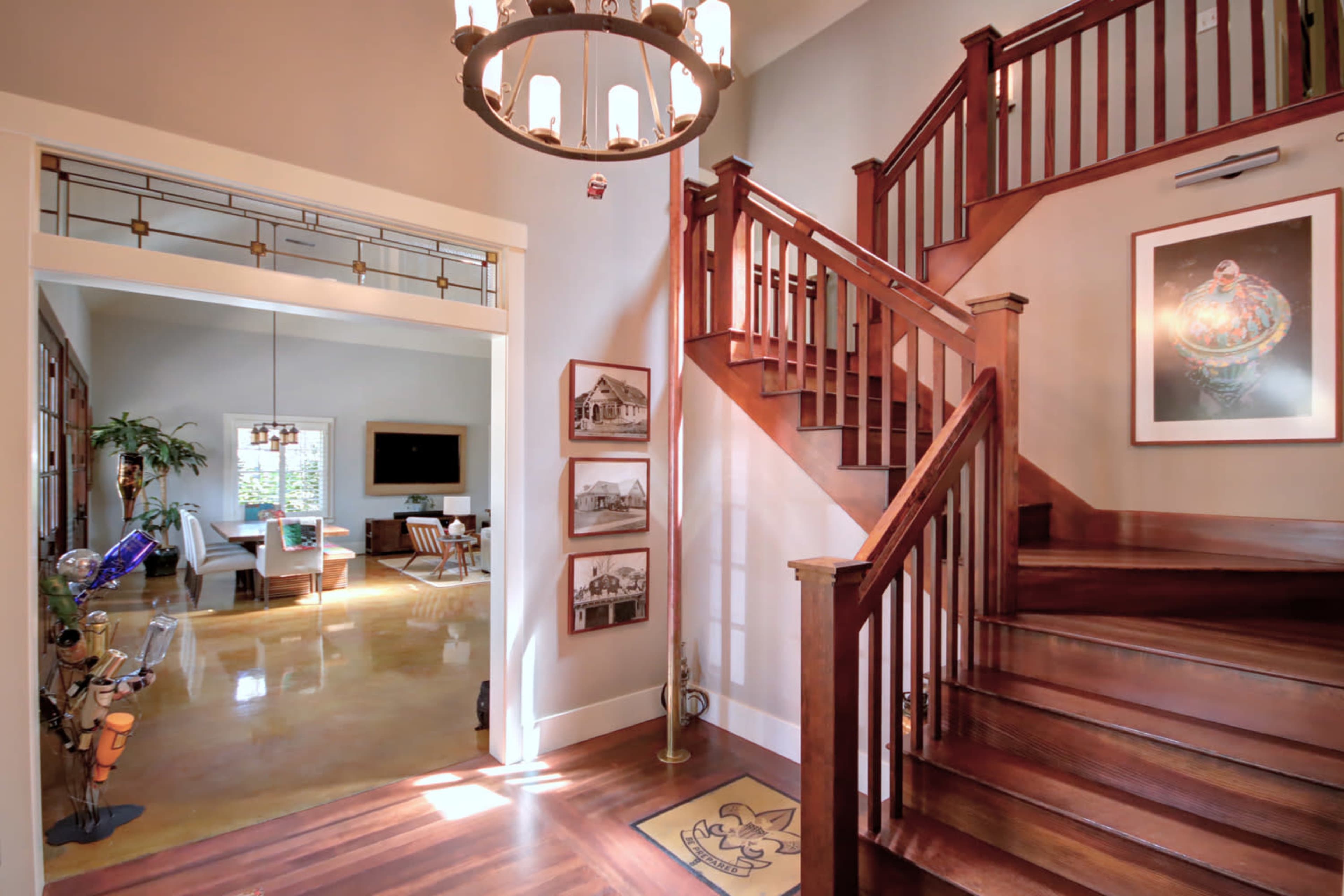 A well-lit entryway with a wooden staircase, framed pictures on the walls, and a view of a living area beyond.
