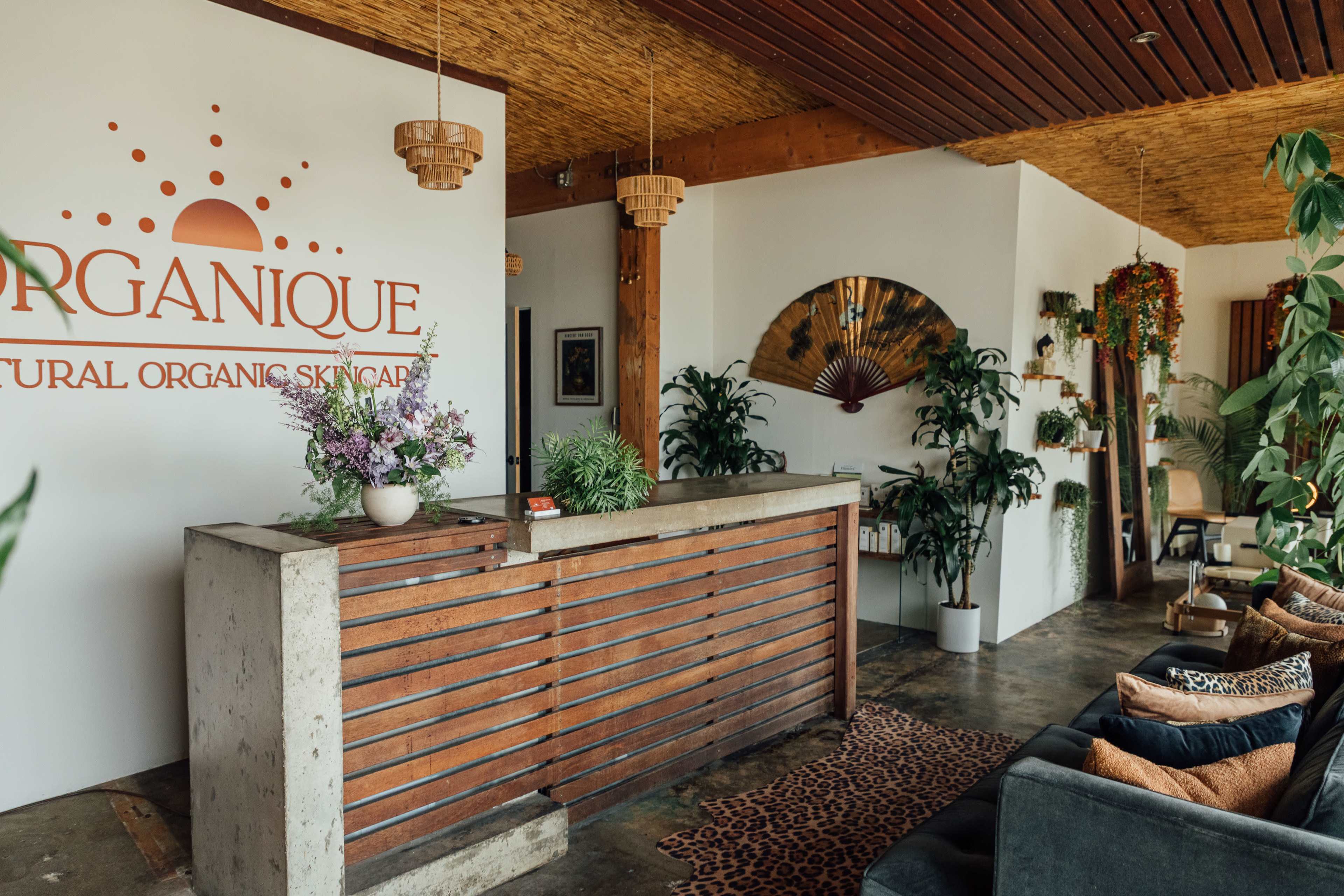 The image shows a modern skincare reception area featuring a wooden counter, potted plants, and decorative elements on the walls and ceiling.