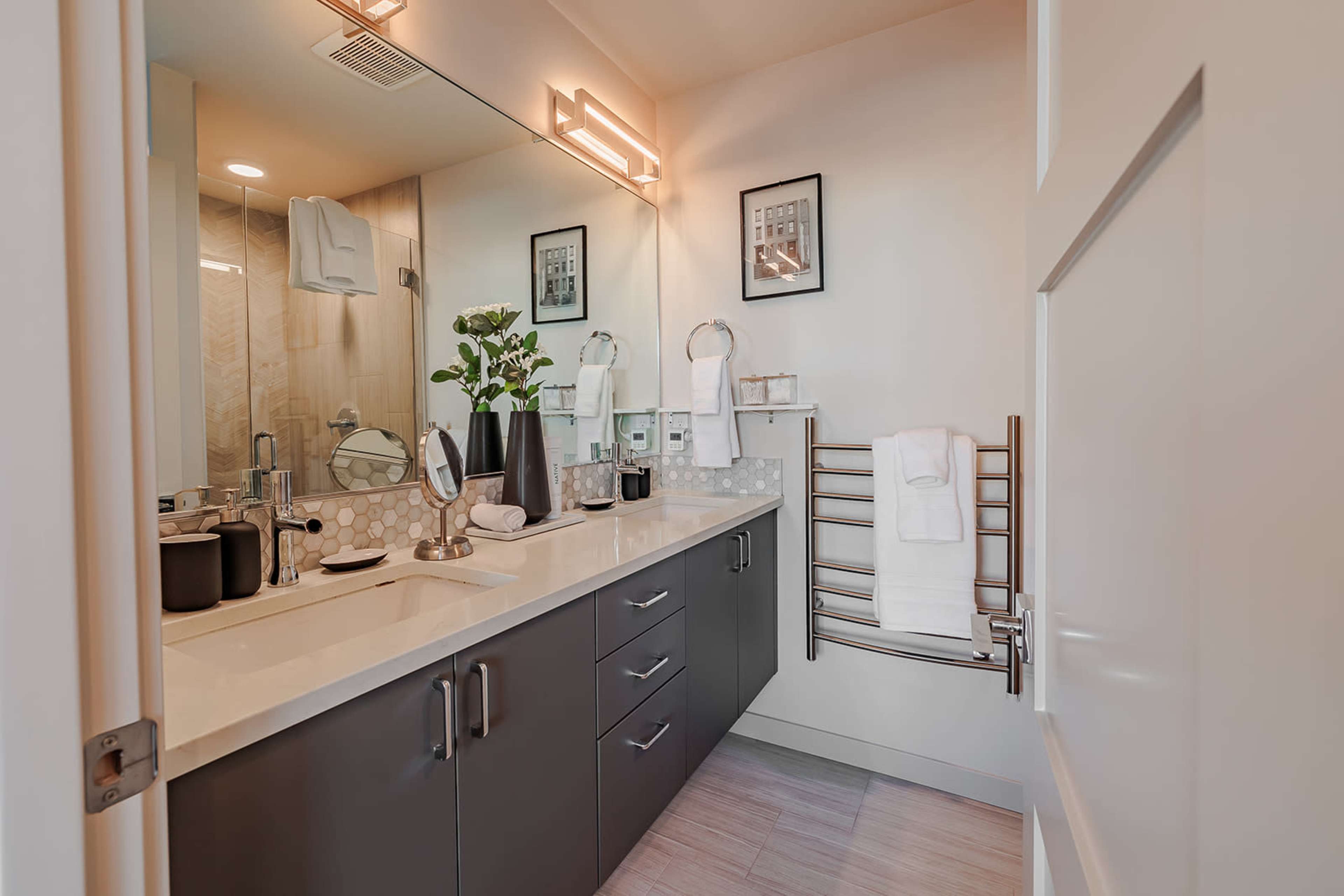 The image shows a modern bathroom with a sleek double-sink vanity, a mirror above the sink, and neatly organized towels on a rack.