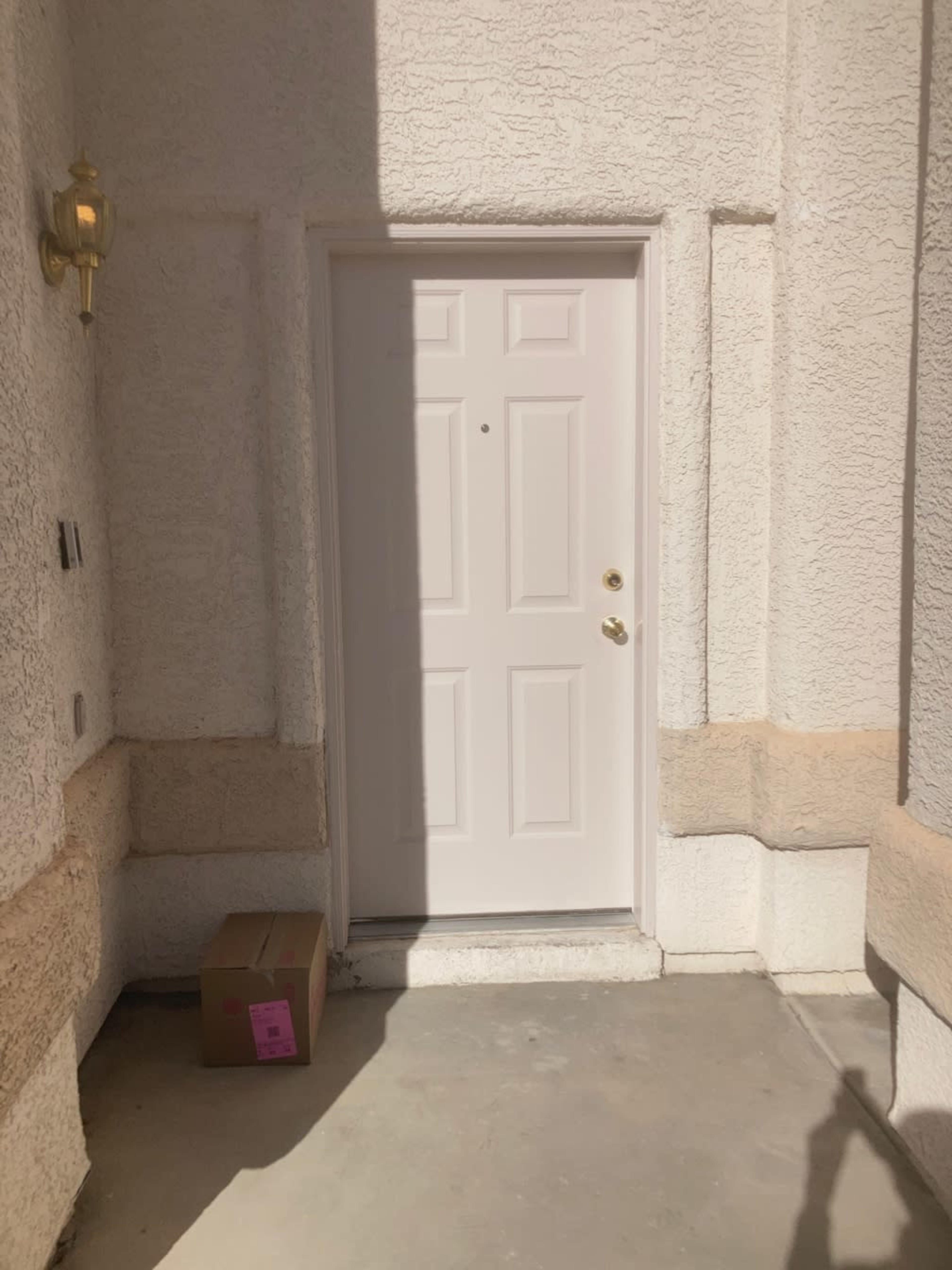 A white door is centered in a light-colored wall with a small box on the ground in front of it.