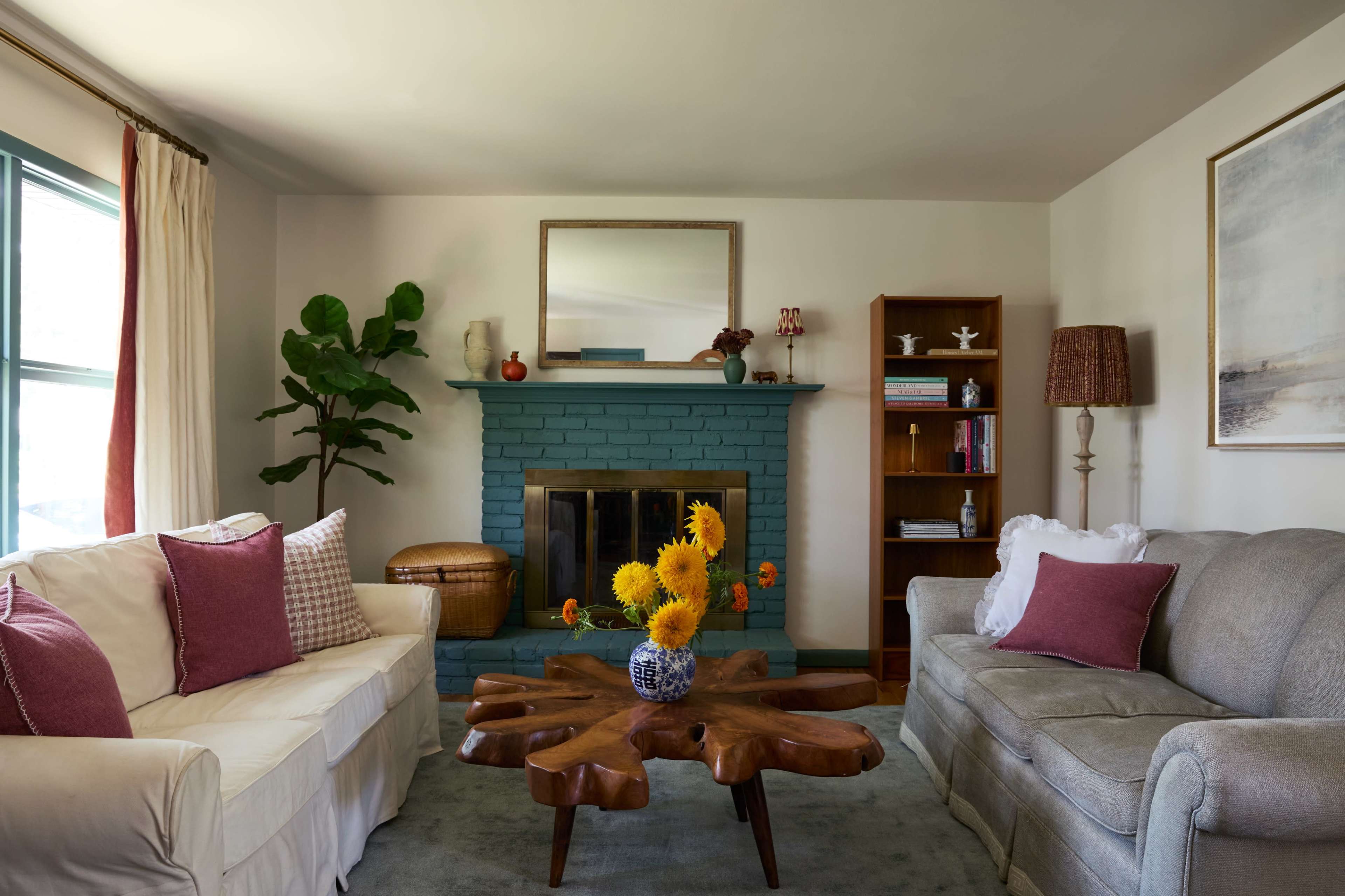 The living room features two sofas, a wooden coffee table with a unique design, a teal-colored fireplace, and bookshelves with decorative items.