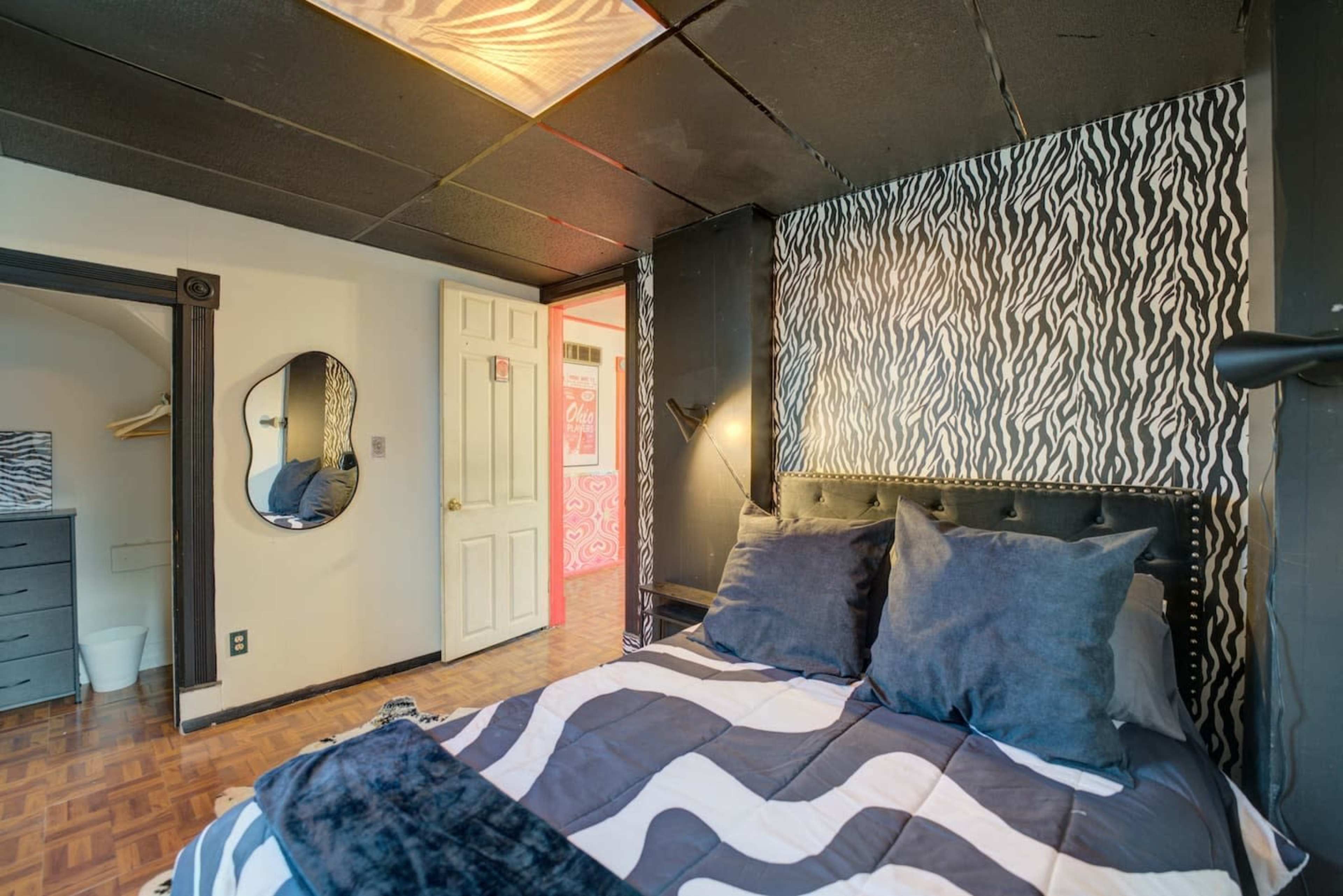 The image shows a bedroom featuring a patterned wall, a bed with gray and white bedding, and a decorative mirror on the wall.