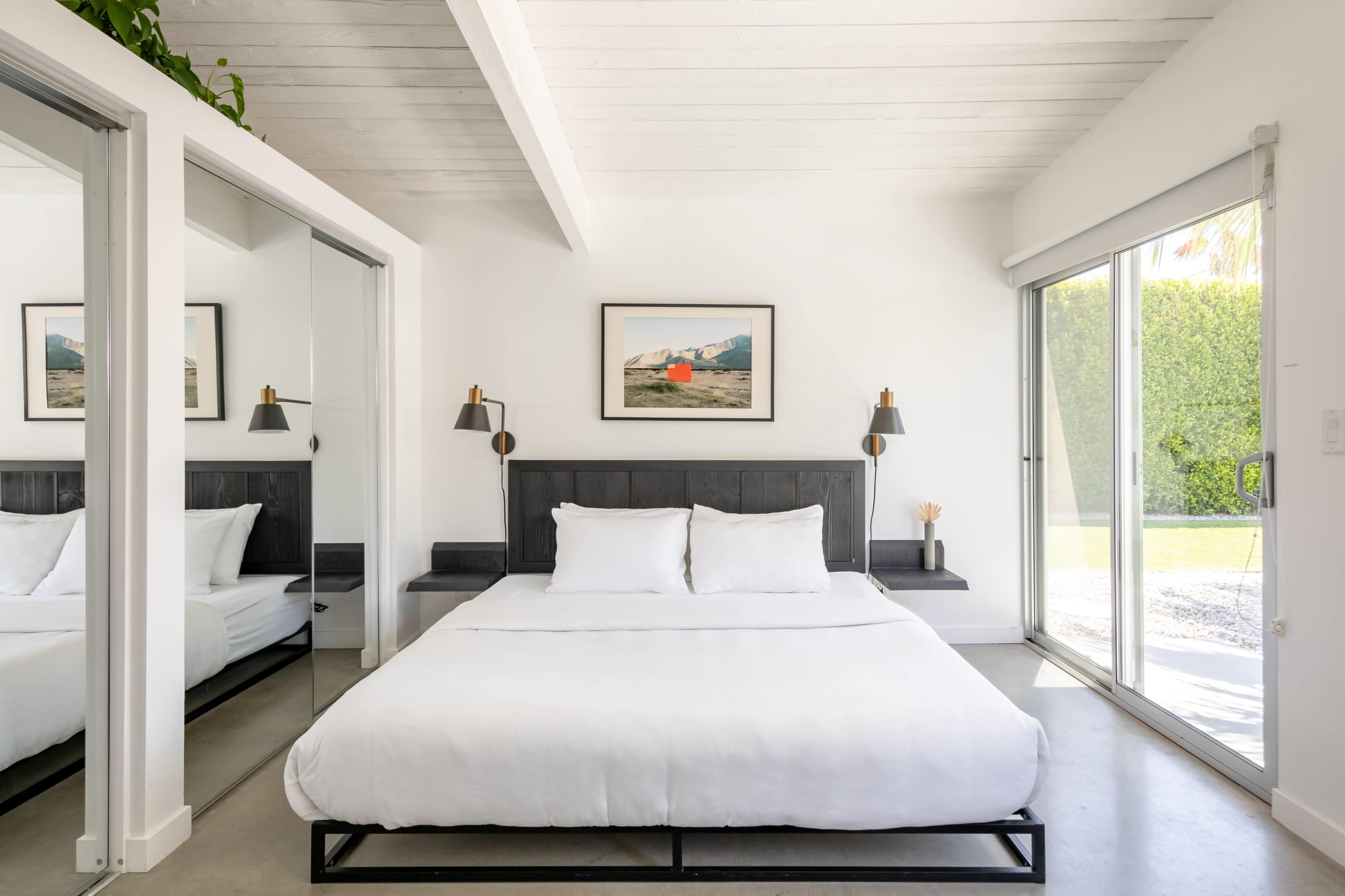 A modern bedroom features a bed with white linens and a large window that opens to an outdoor view.