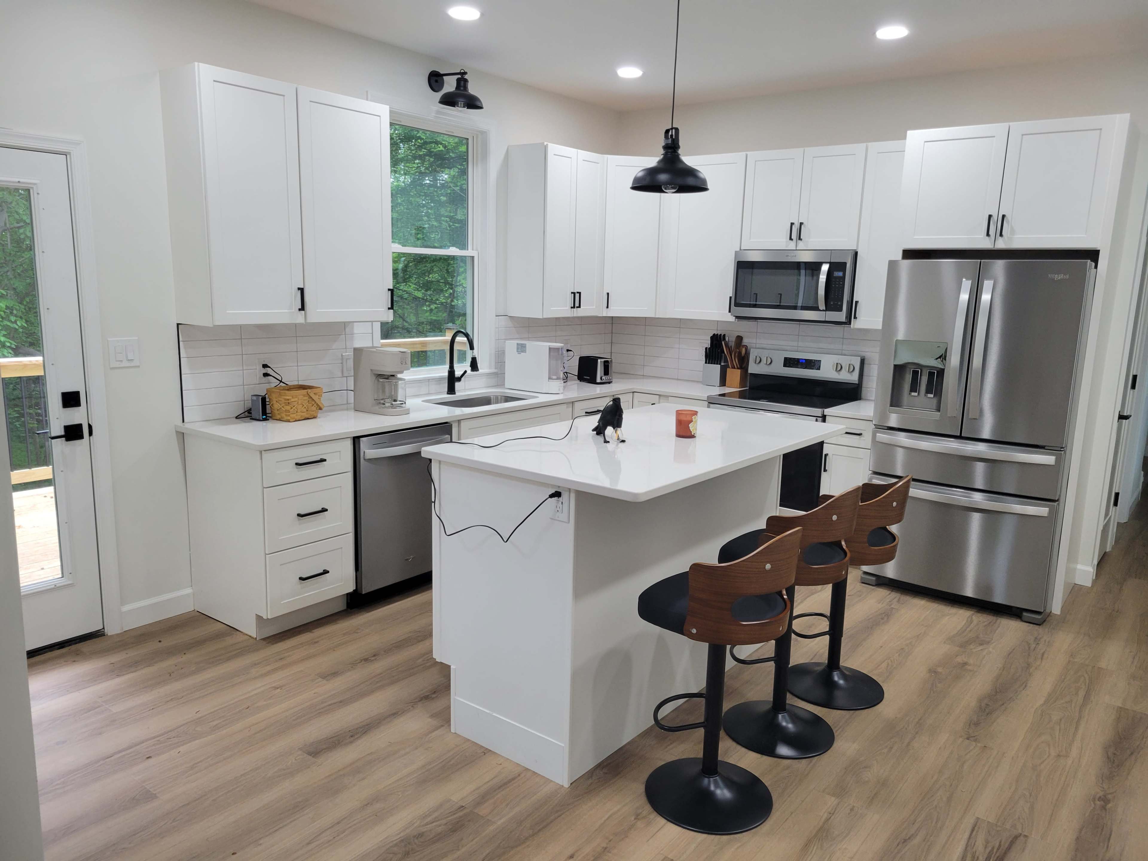 The image shows a modern kitchen with white cabinets, stainless steel appliances, and a center island with bar stools.