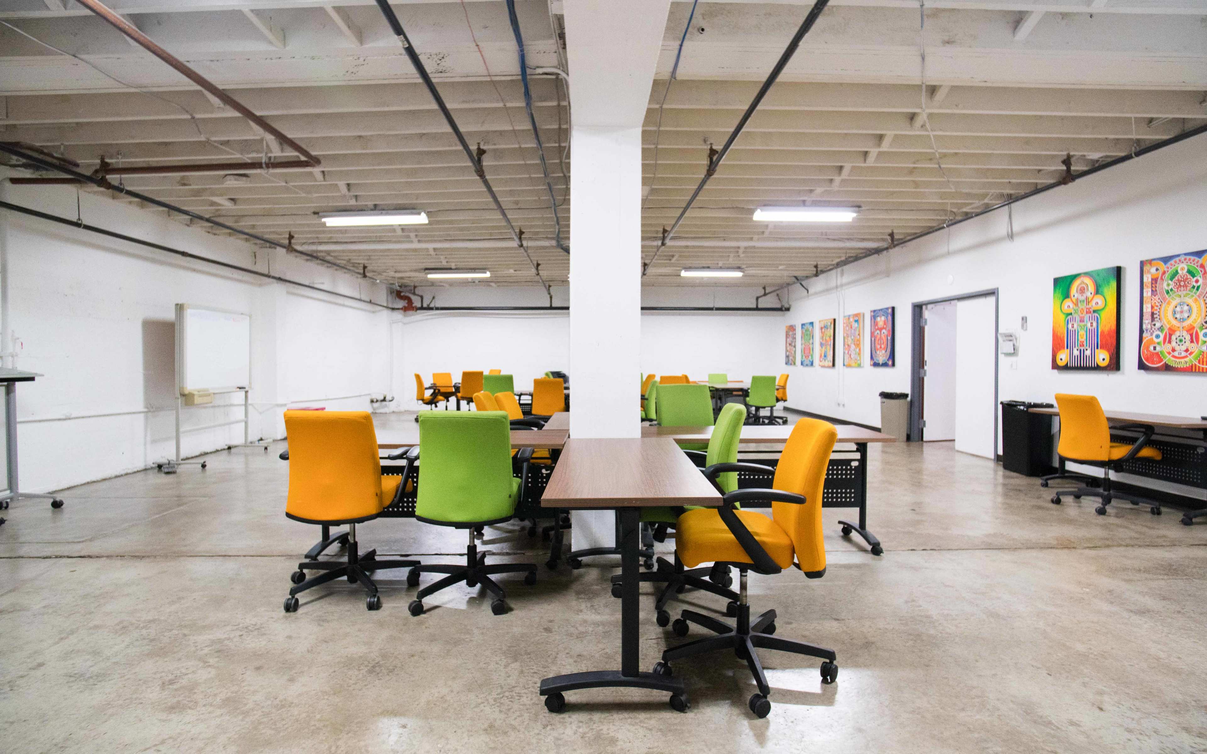 A spacious, empty office area with several tables and colorful chairs arranged around them.